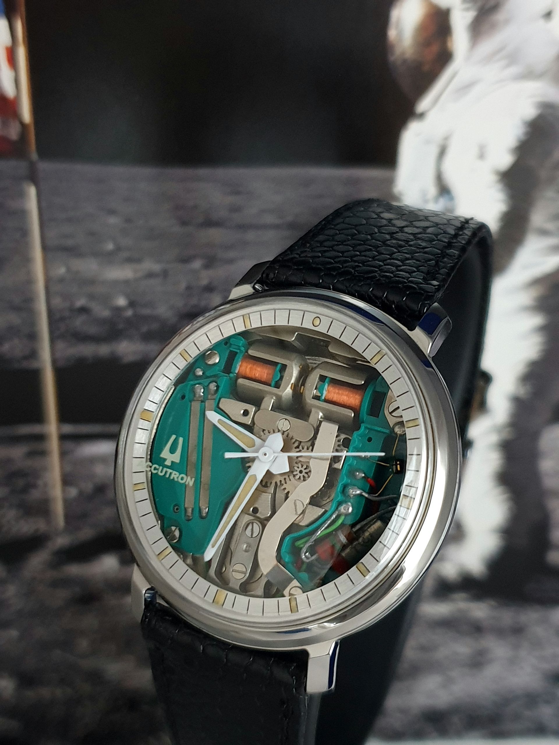 Close-up of a silver skeleton wristwatch with a green dial and black strap on a dark surface