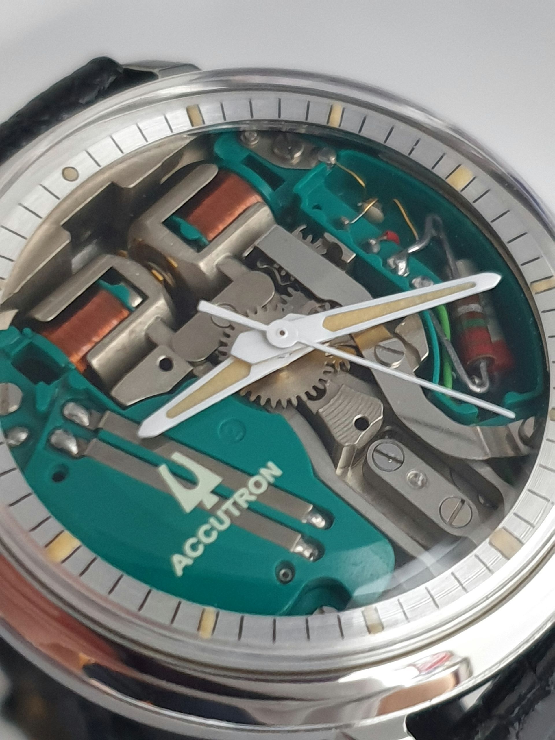 Close-up of a silver and green skeleton wristwatch with white hands and visible gears