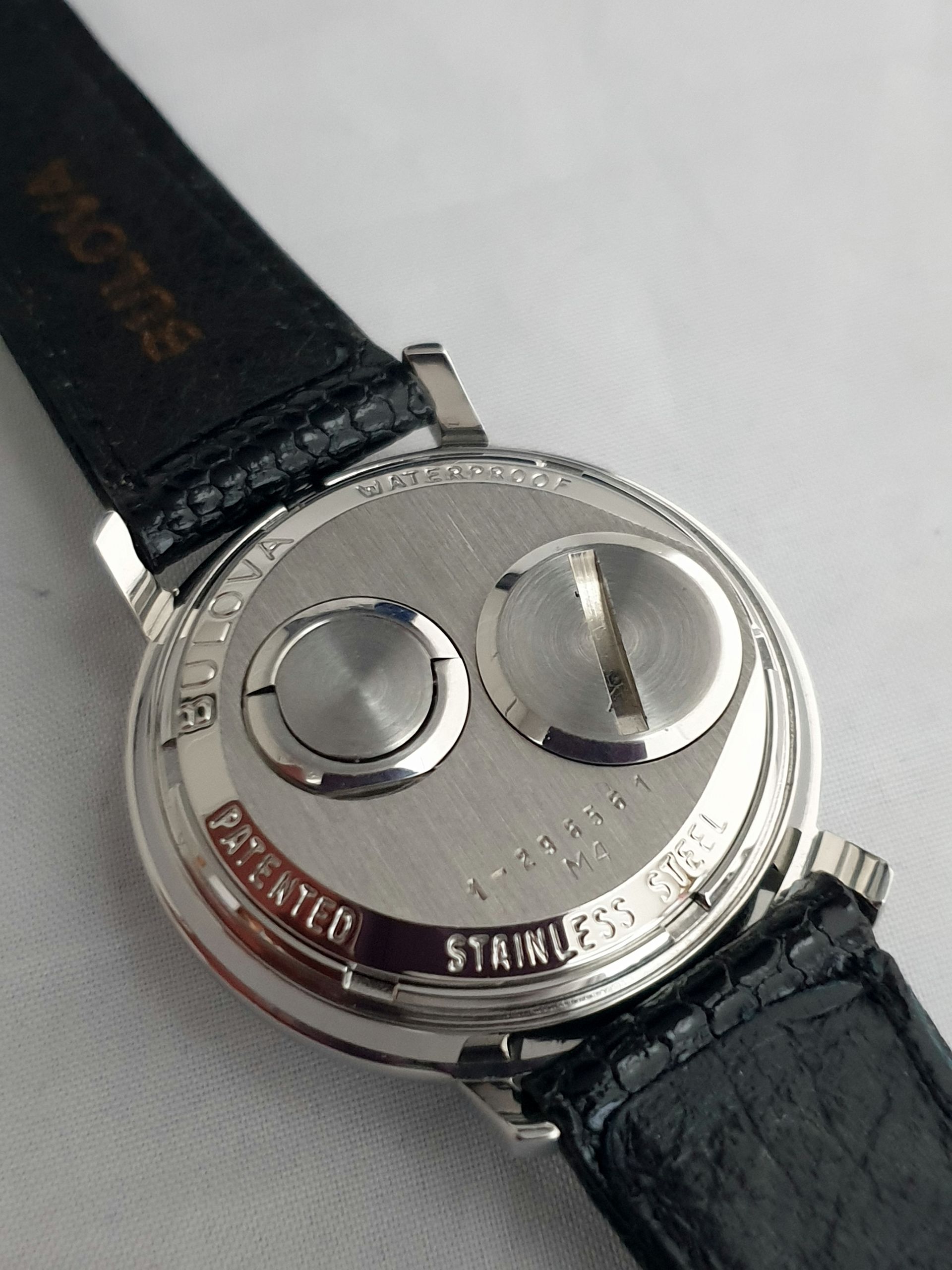 Close-up of a silver watch back with black leather strap and engraved “Stainless Steel” text