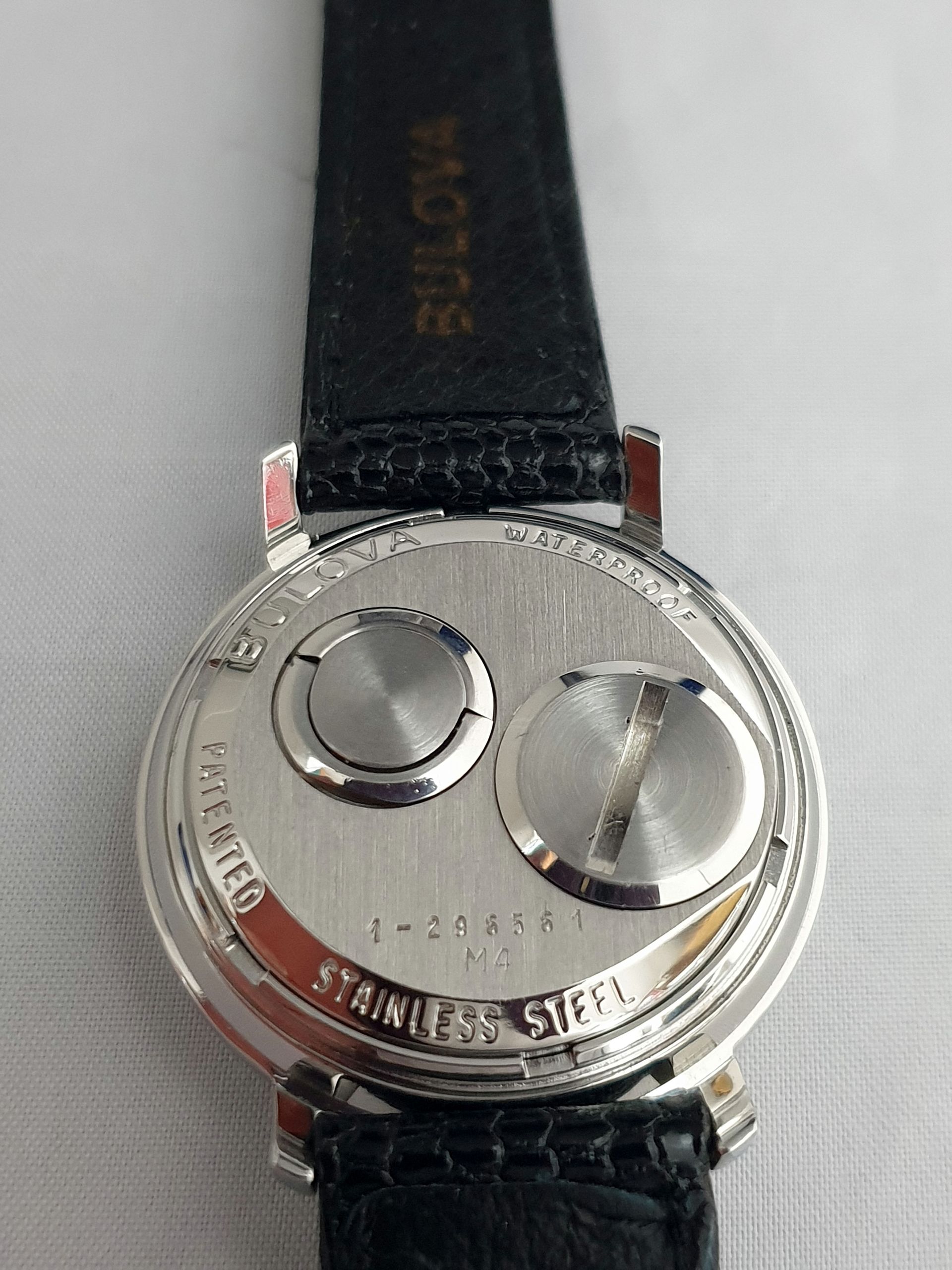 Close-up of a silver wristwatch back with black leather strap and engraved metal case.