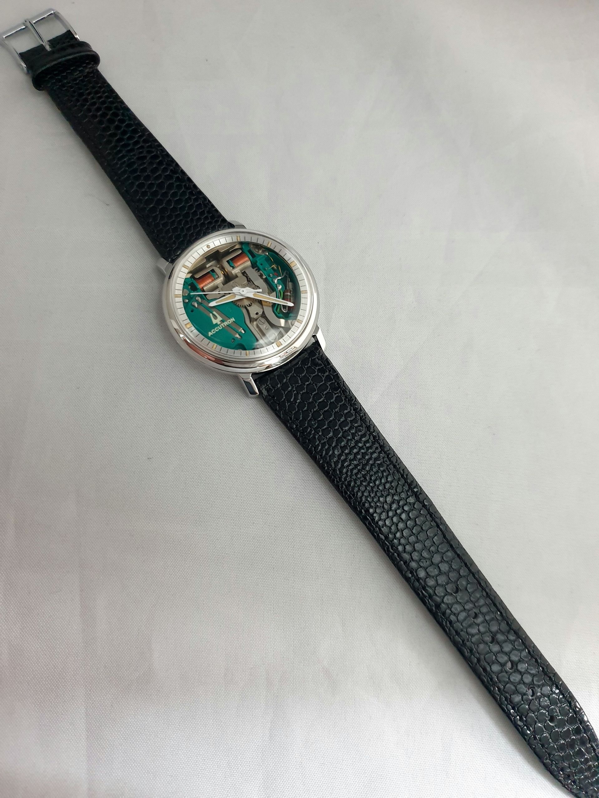 Black wristwatch with a green face and silver bezel on a light fabric background