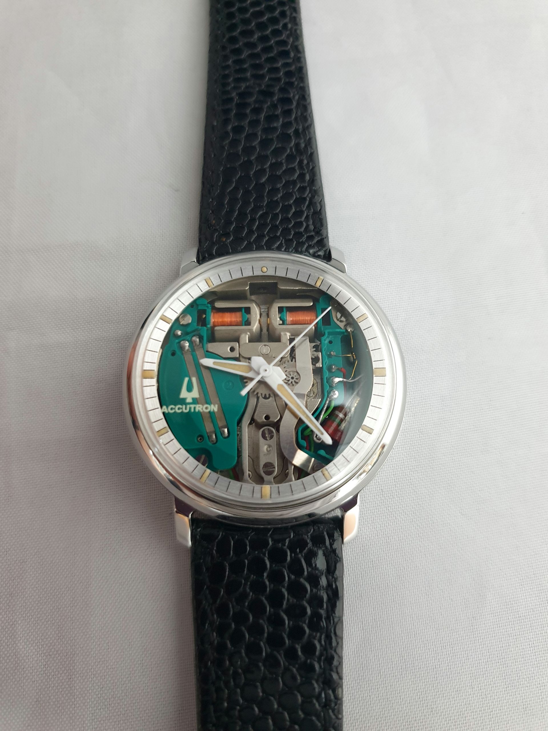 Silver wristwatch with exposed mechanical face and black textured strap on a light background