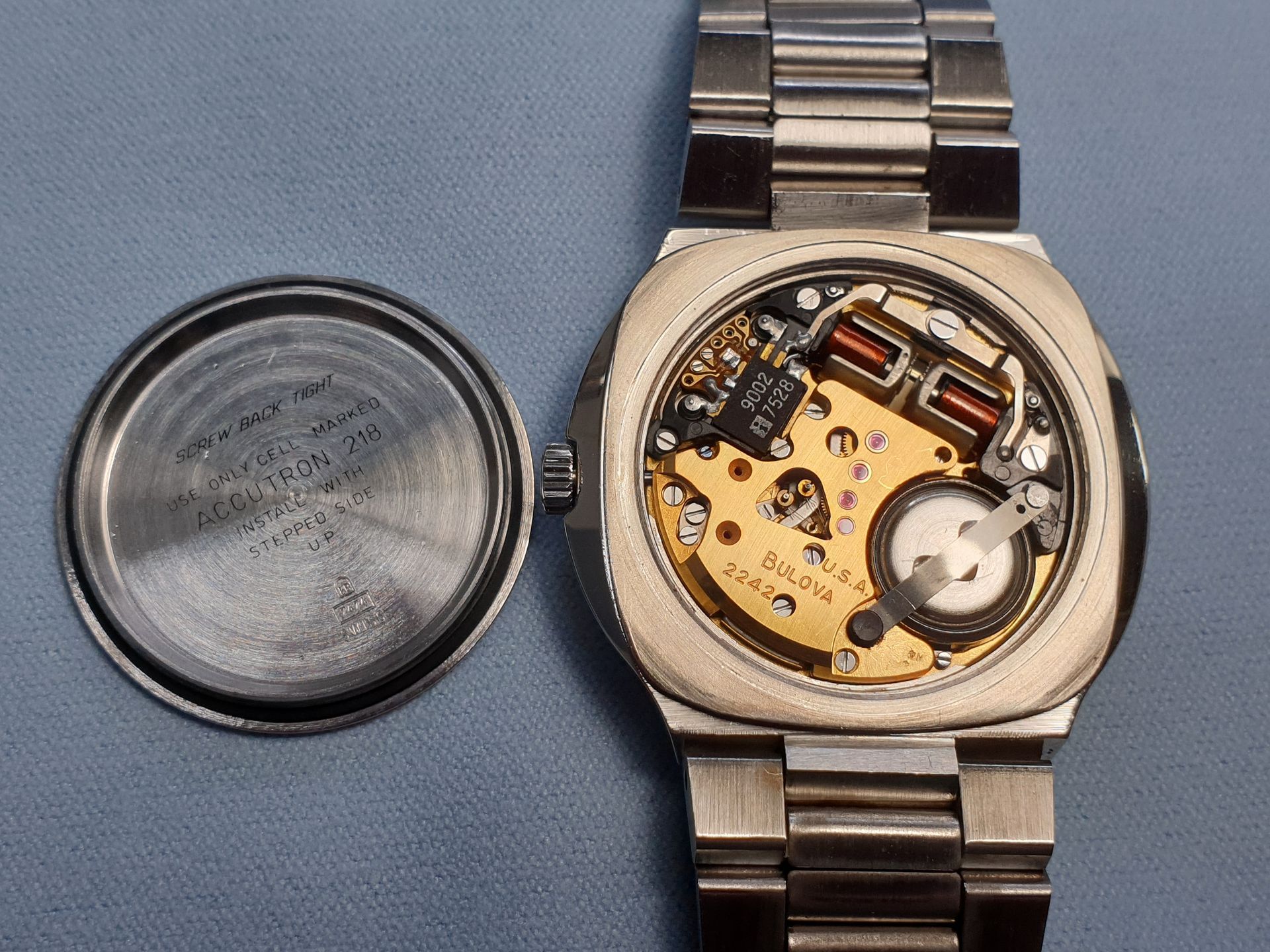 Open wristwatch with exposed mechanical movement and steel band beside its detached case back