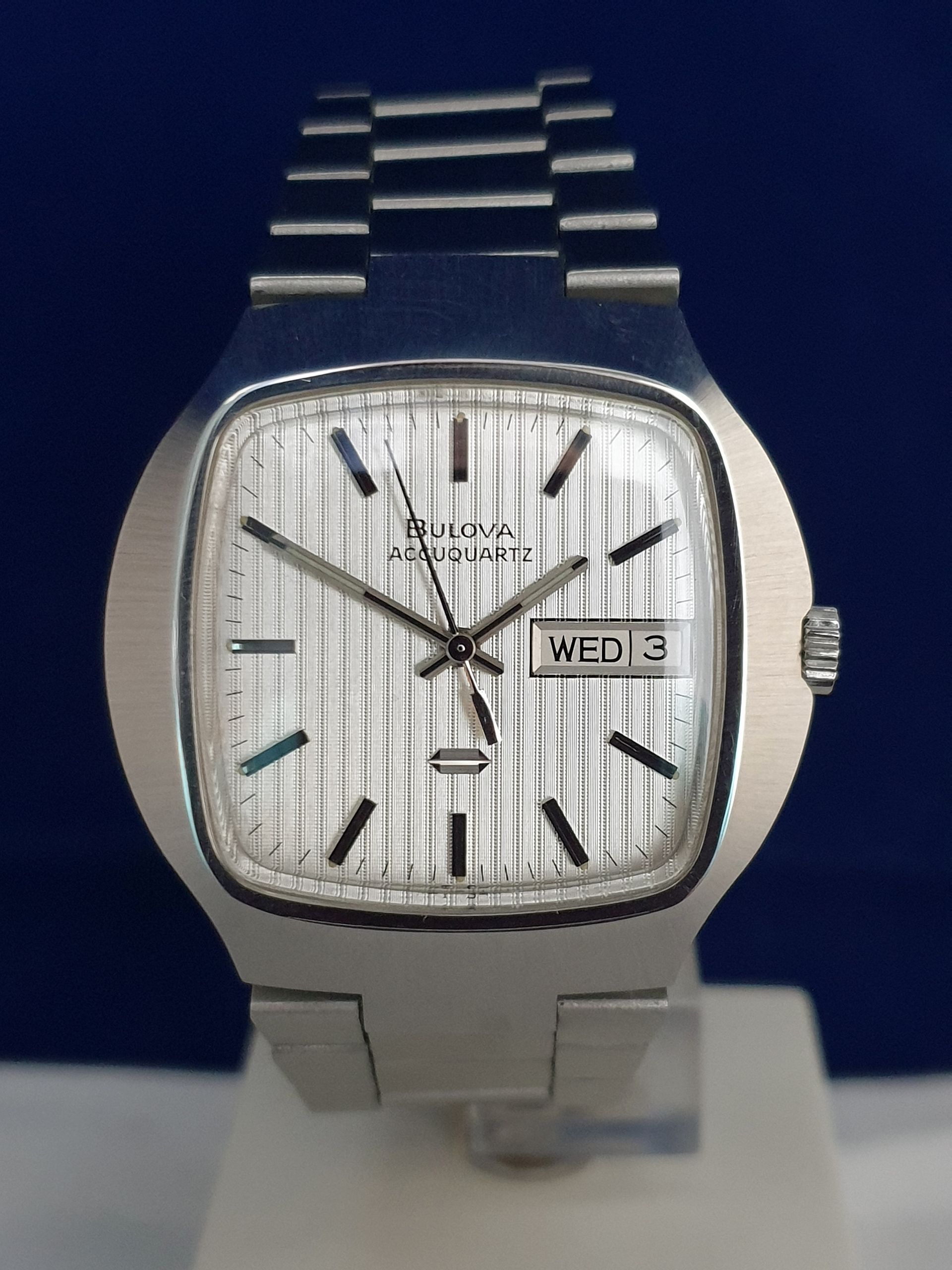 Silver Bulova wristwatch with white dial and metal band, showing Wednesday 3 on the date display.