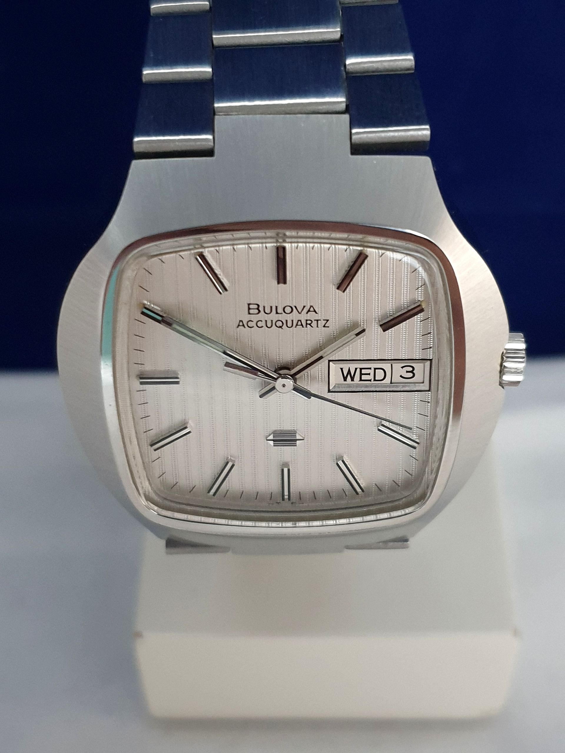 Bulova Accutron wristwatch with silver dial and metal band on a display stand, showing Wed 3