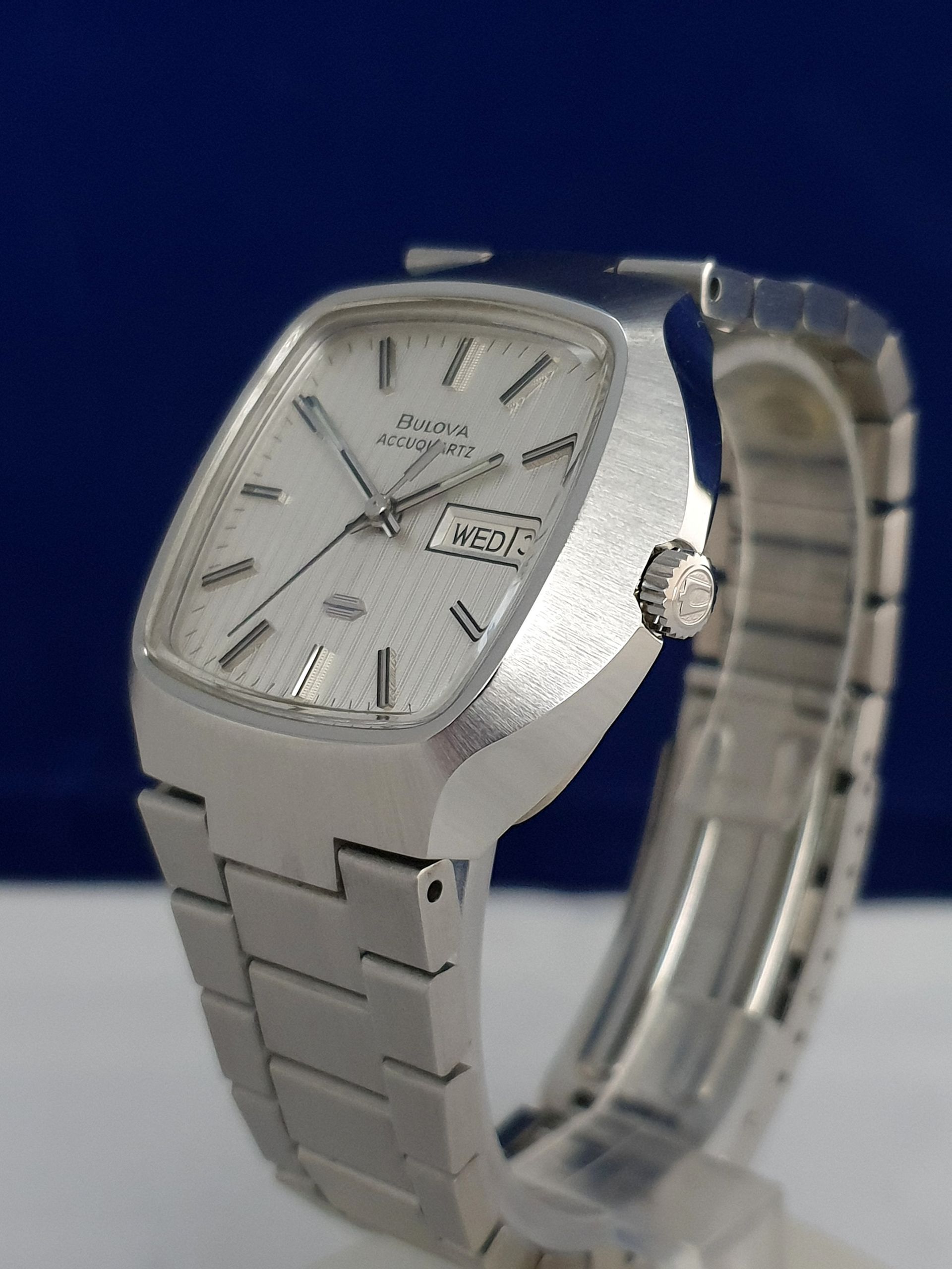 Silver wristwatch with metal band and square face on a blue background