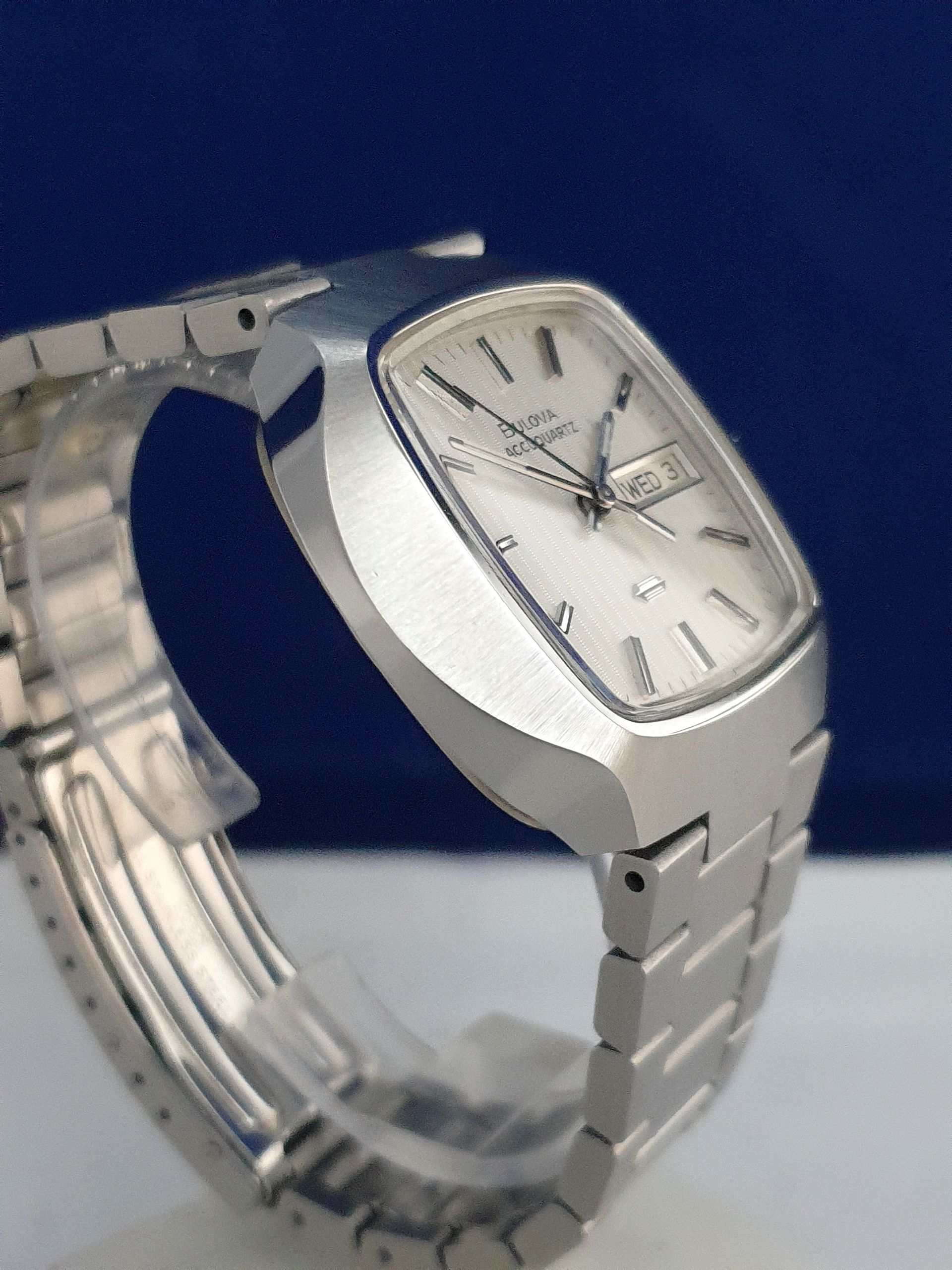 Silver metal wristwatch with a white face and link band on a blue background