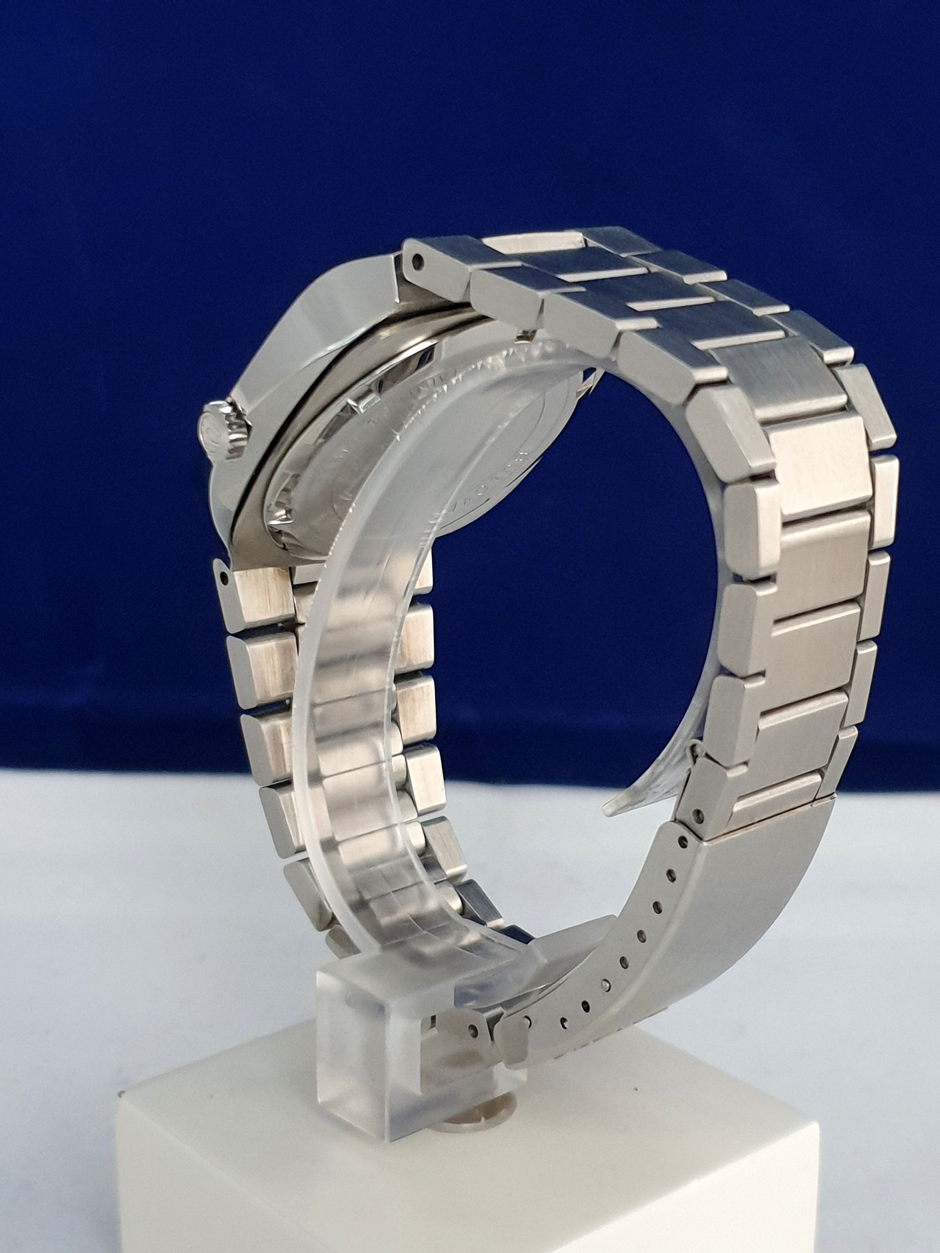 Silver metal wristwatch displayed on a clear stand against a blue background
