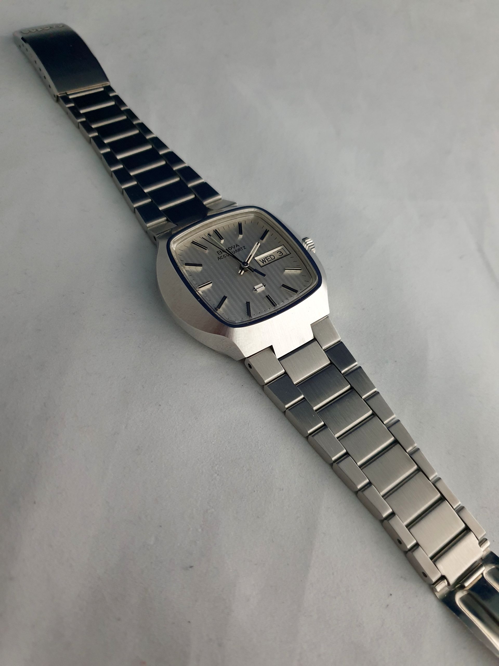Silver wristwatch with dark face and metal band on a light gray surface