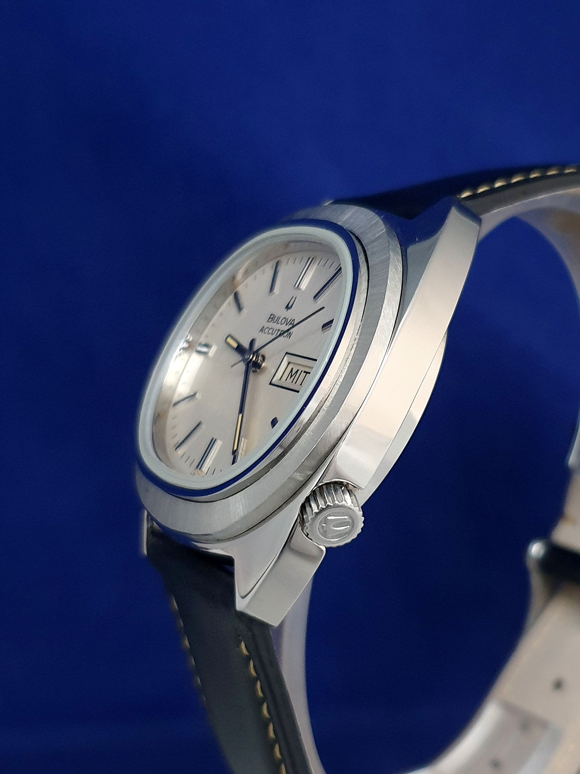 Silver wristwatch with white dial and black strap on a blue background