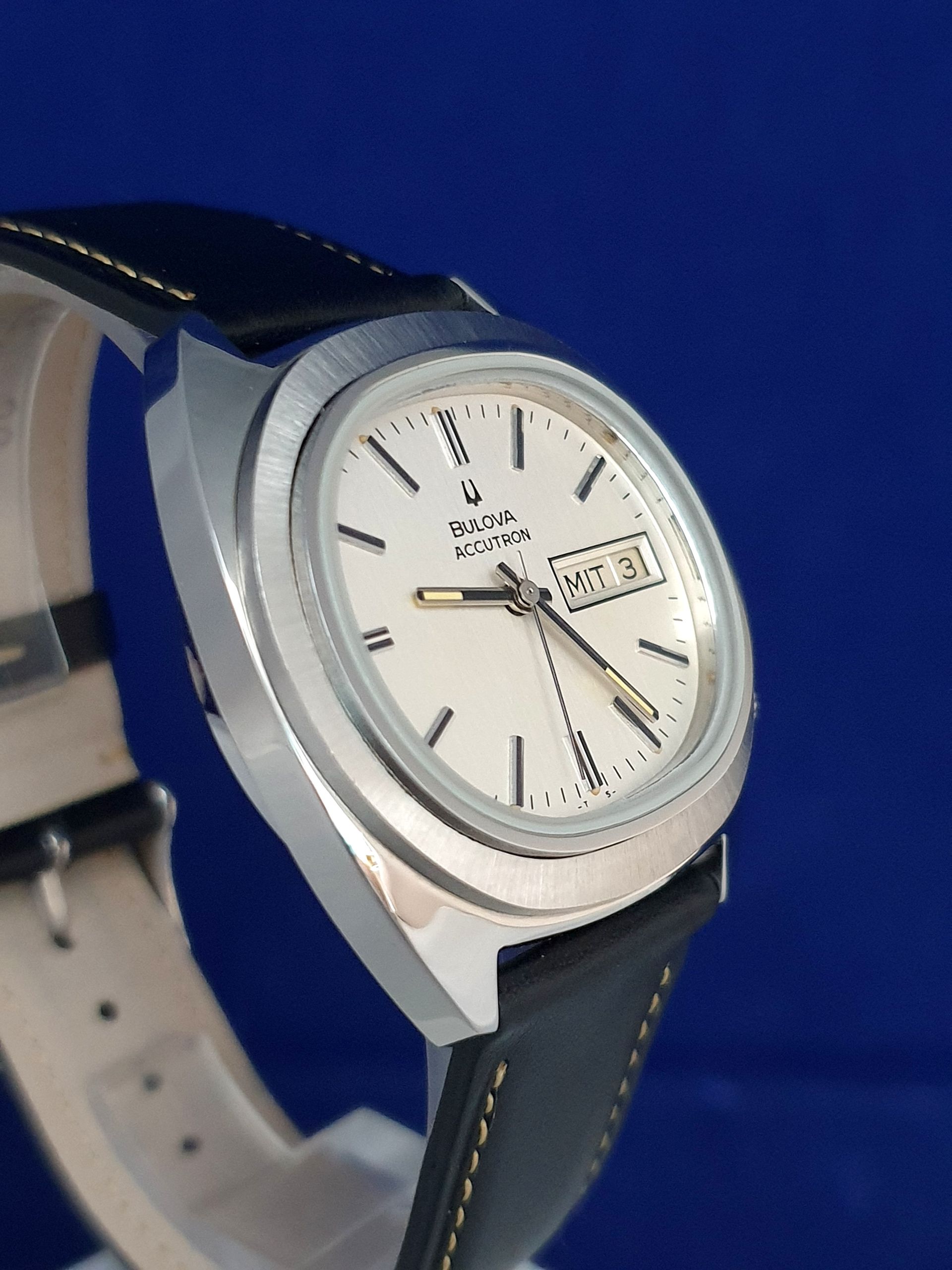 Close-up of a silver analog wristwatch with black leather strap on a blue background