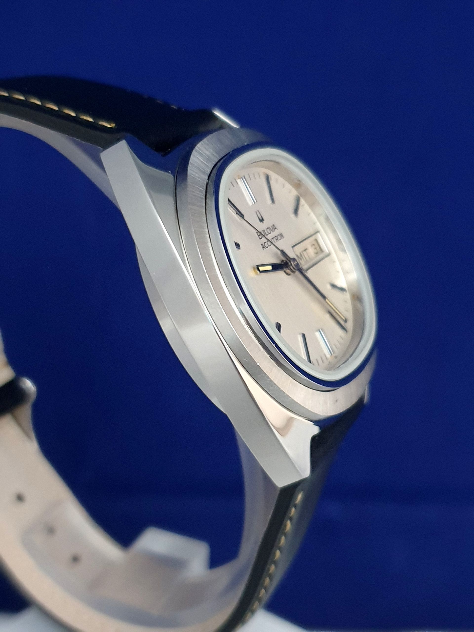 Silver wristwatch with white face and black strap on a blue background