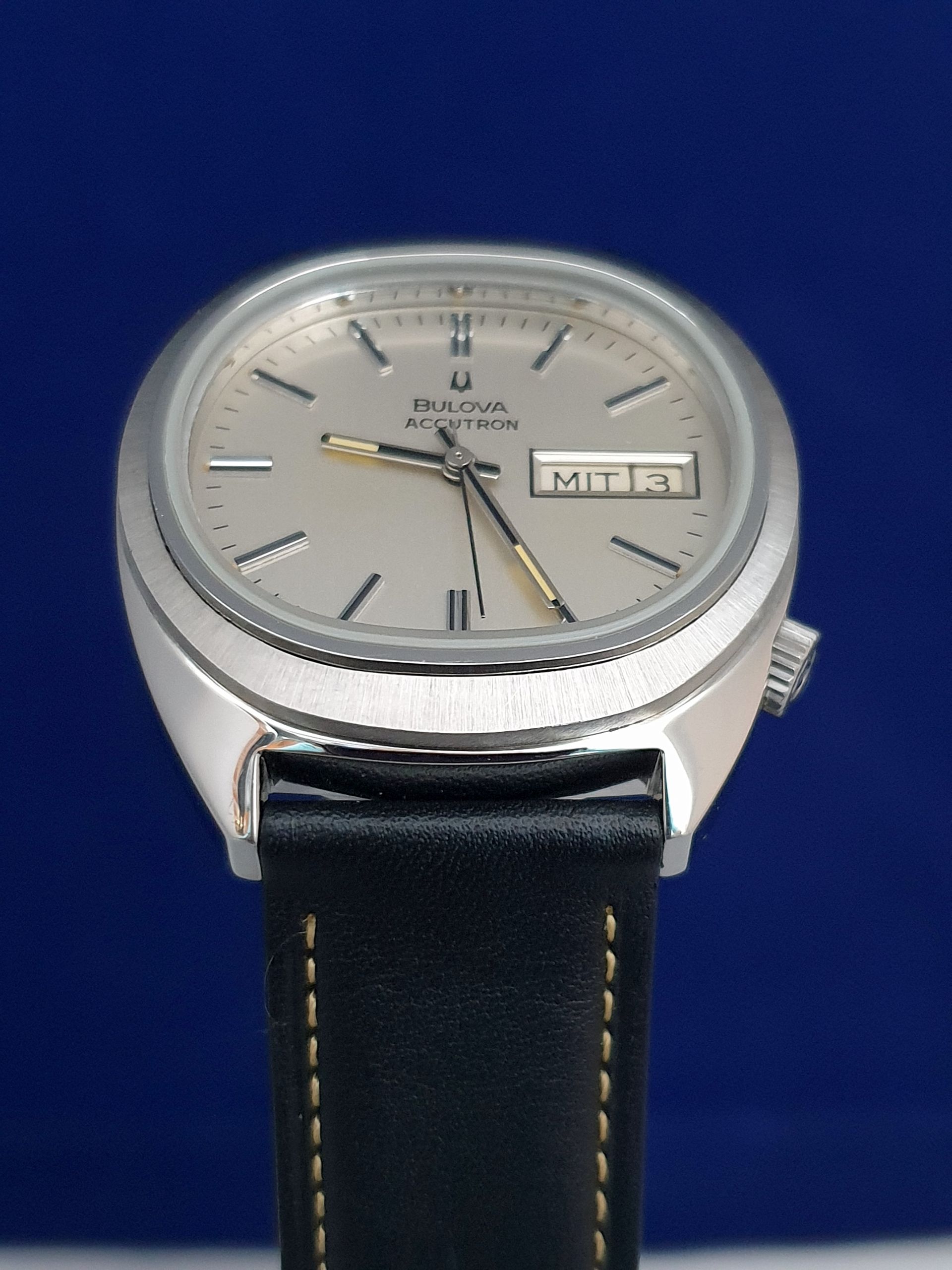 Silver wristwatch with black leather strap and analog-digital dial on a blue background