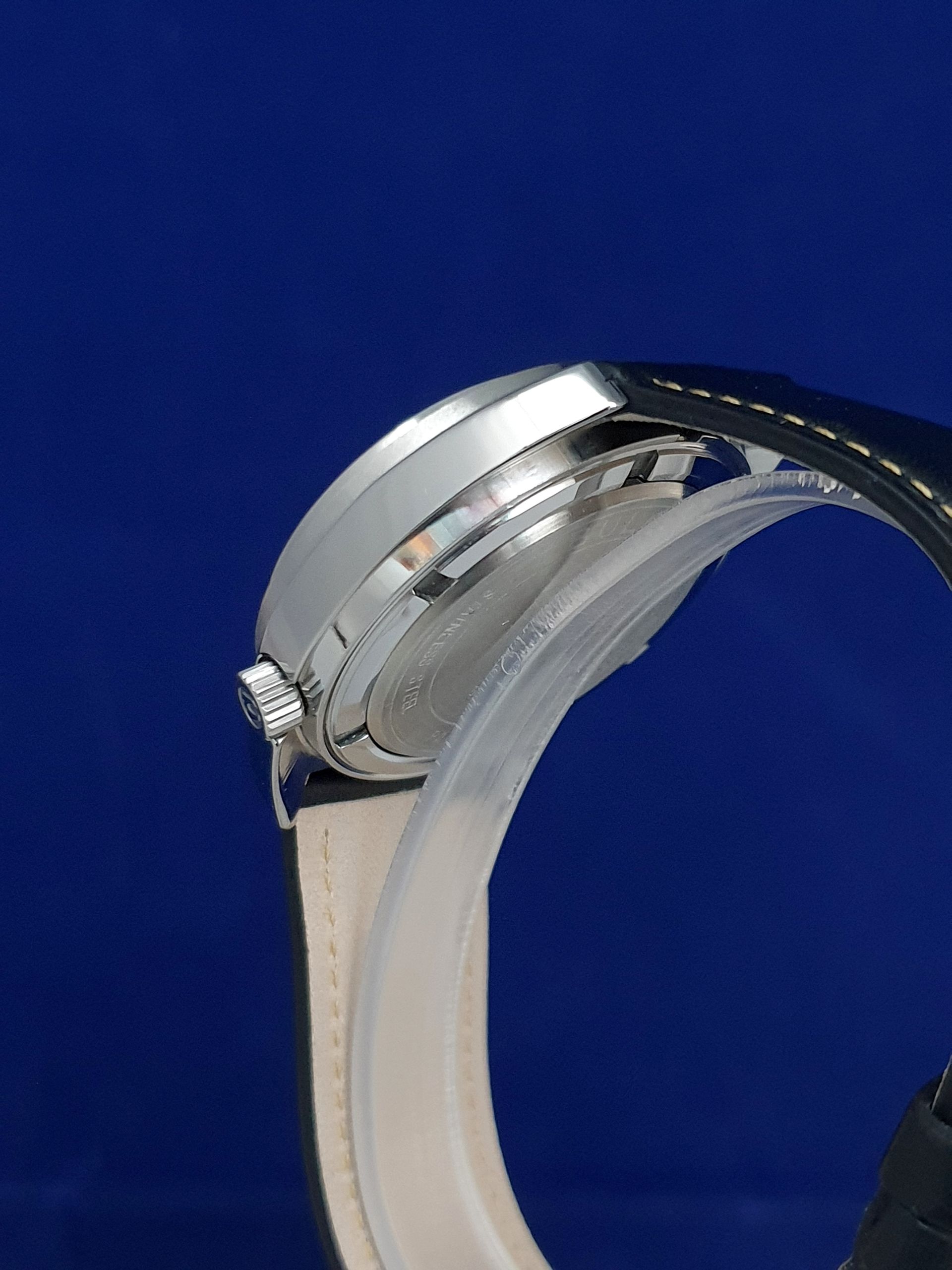 Close-up of a silver wristwatch with a white strap against a blue background