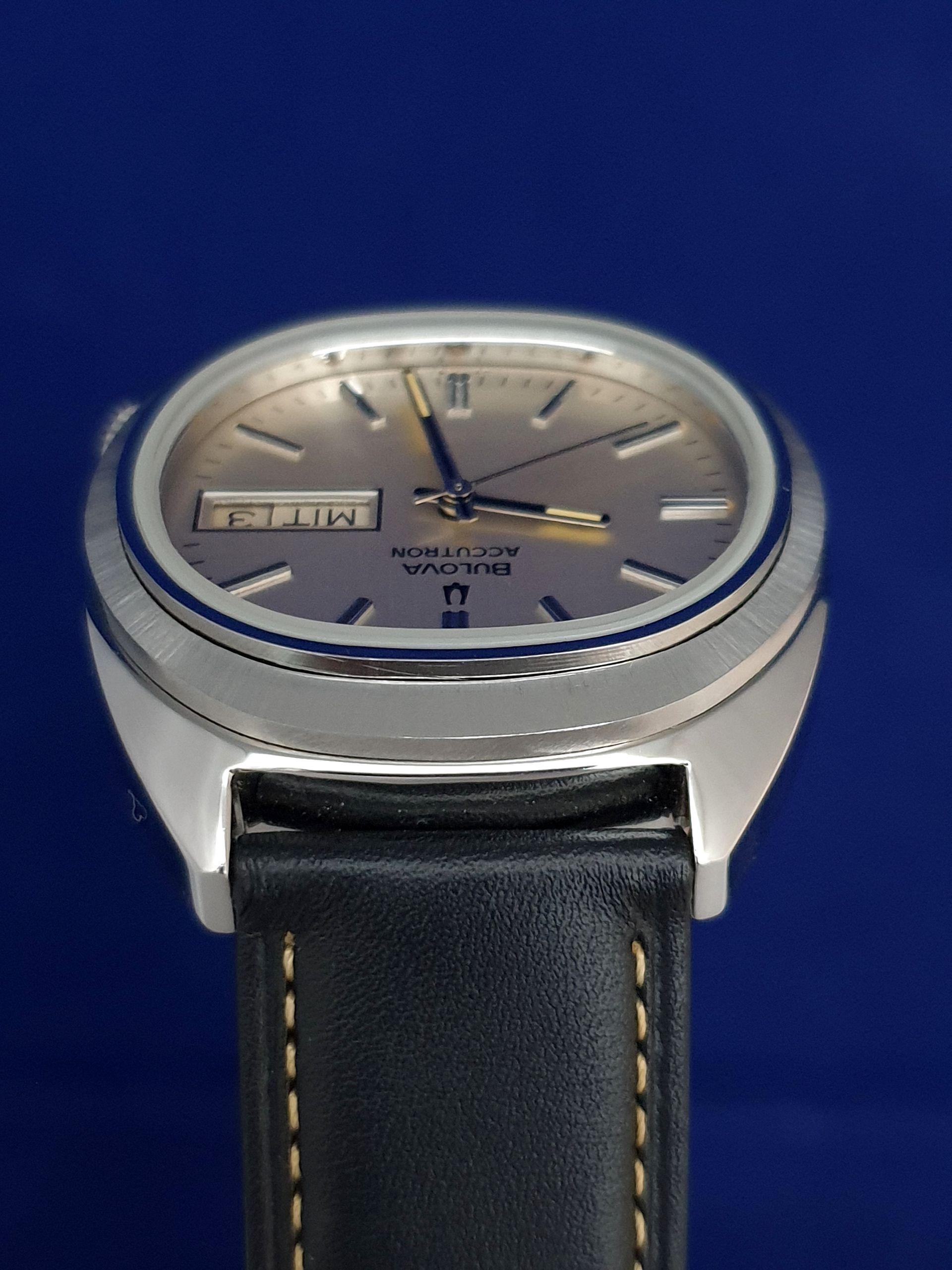 Silver wristwatch with a black leather strap on a blue background