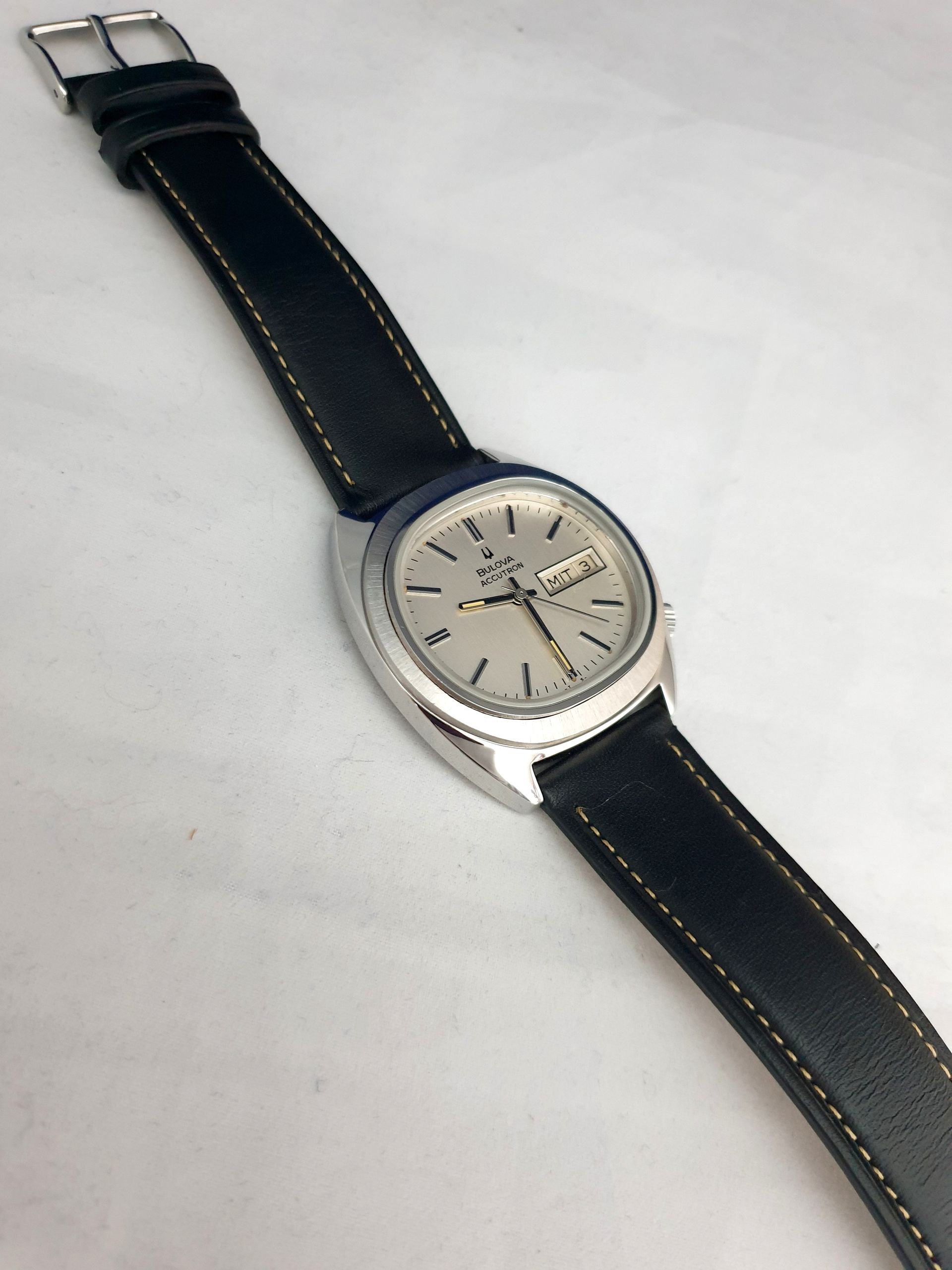 Silver wristwatch with a black leather strap on a light background
