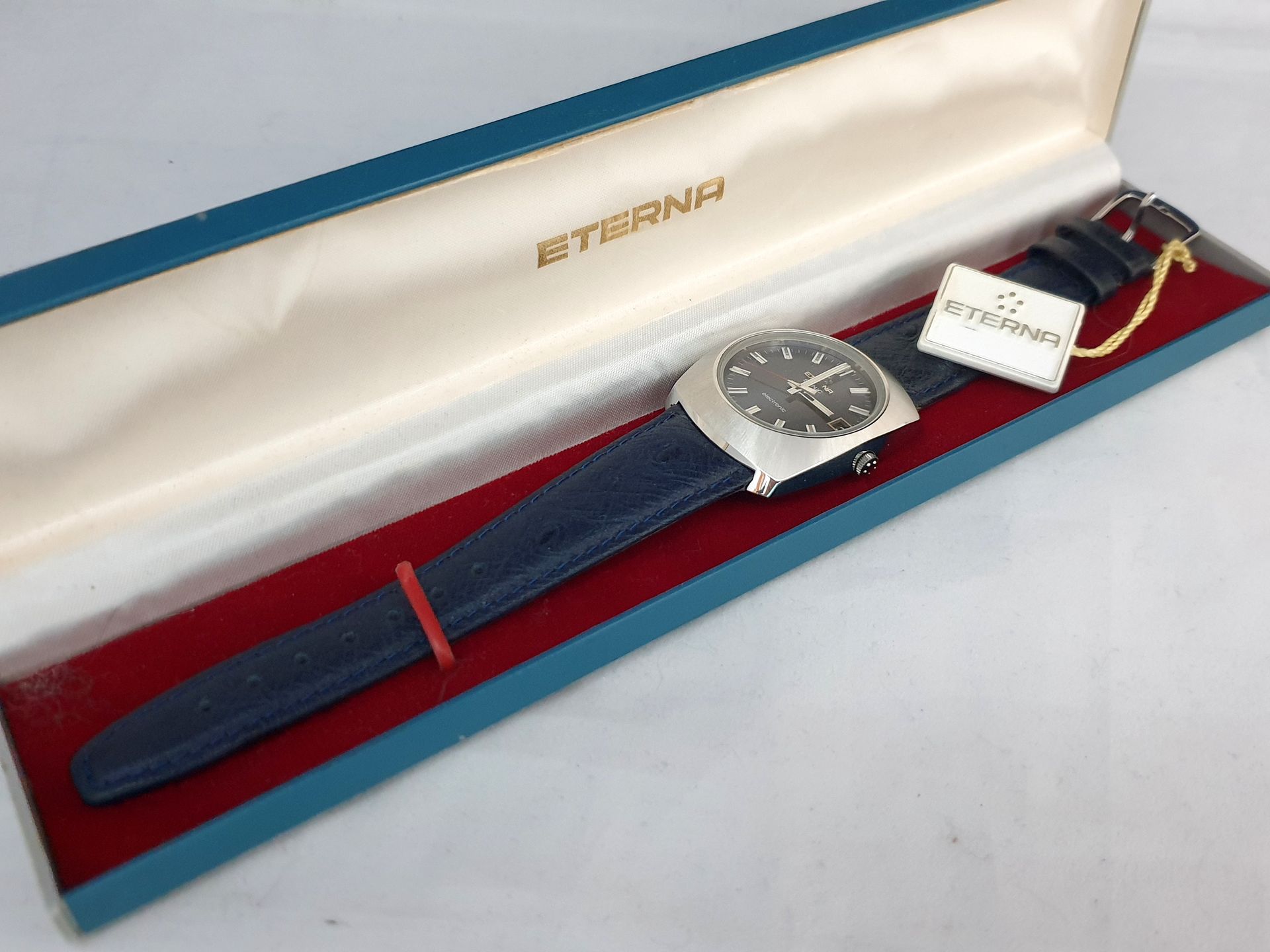 Silver wristwatch with blue strap in red-lined gold watch box
