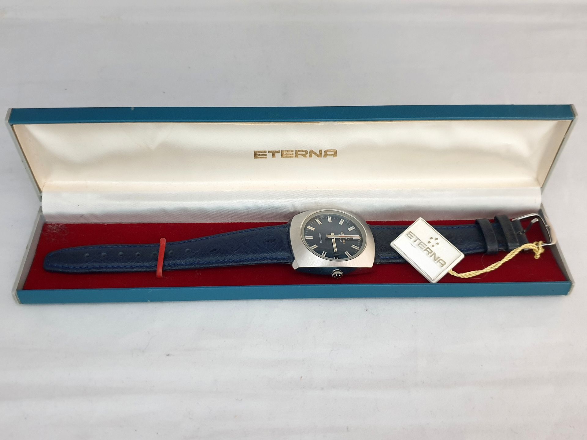 Eterne wristwatch in red presentation box with gold tag and blue strap underneath