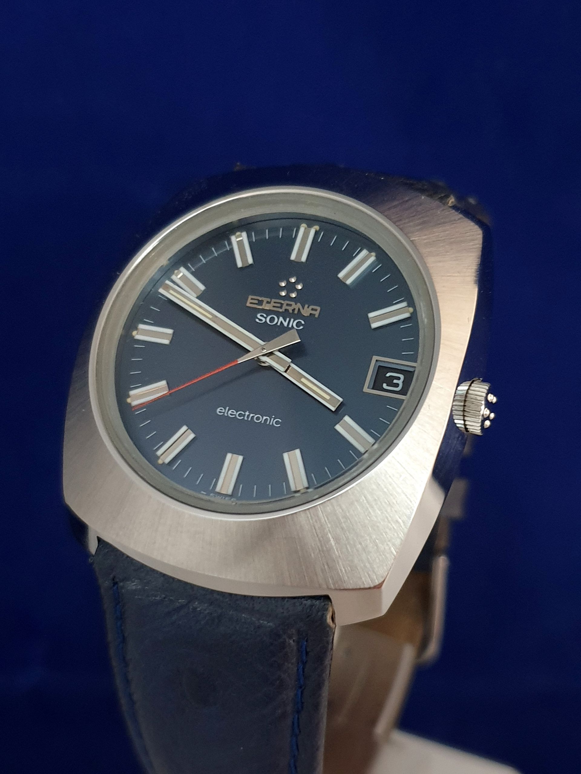 Blue-faced Seiko wristwatch with silver case and dark leather strap on a blue background