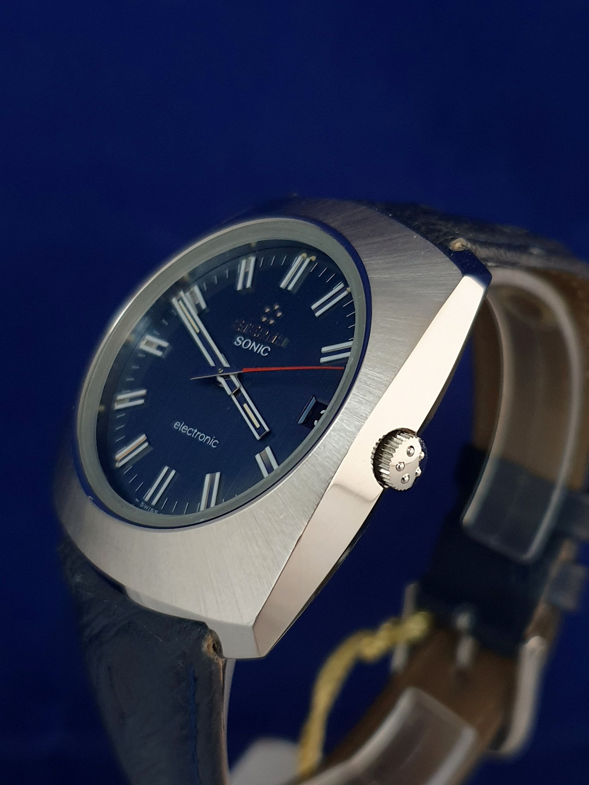 Blue-faced wristwatch with silver case and black leather strap on a blue background