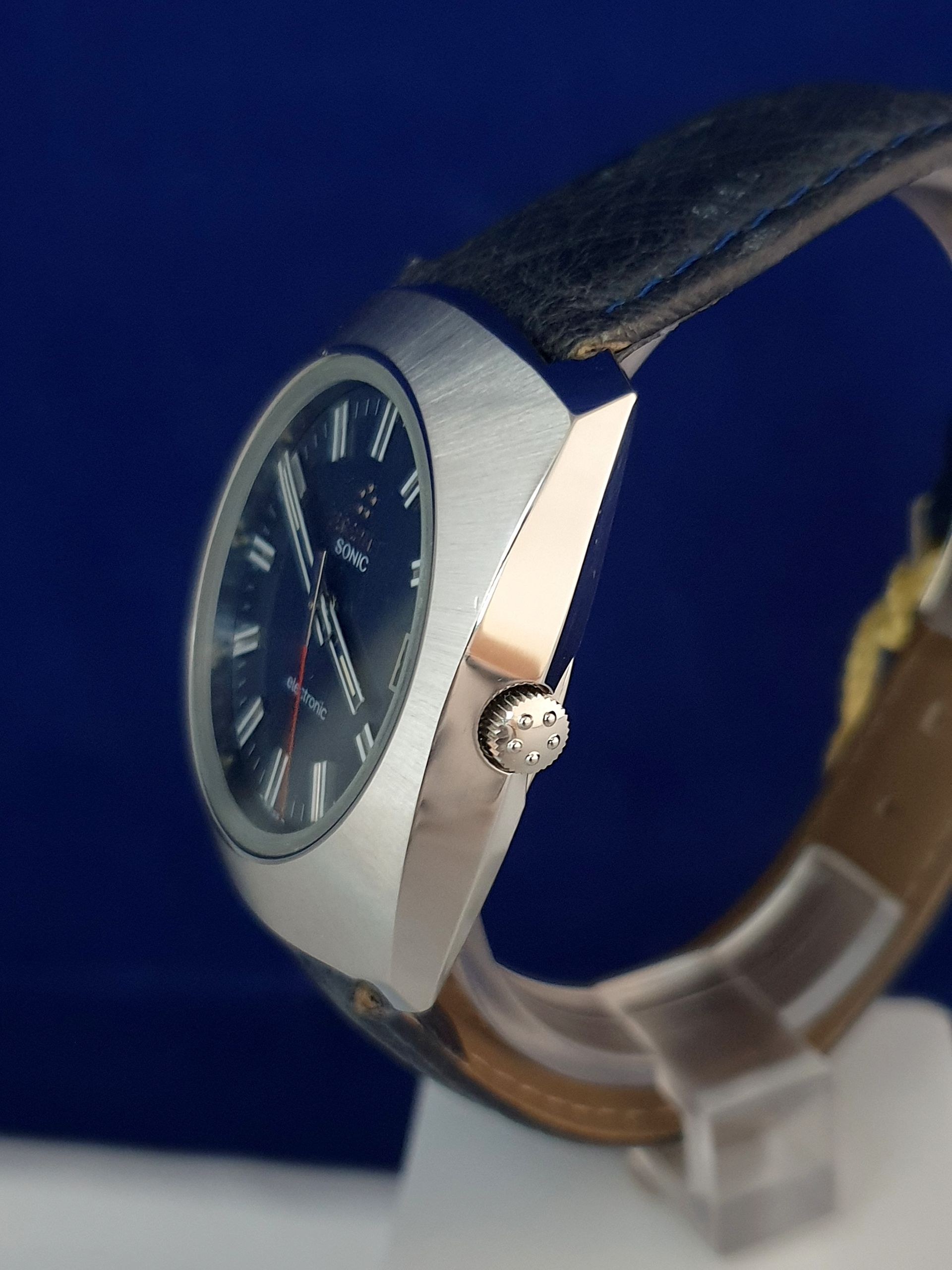 Silver wristwatch with black face and brown leather band on a display stand