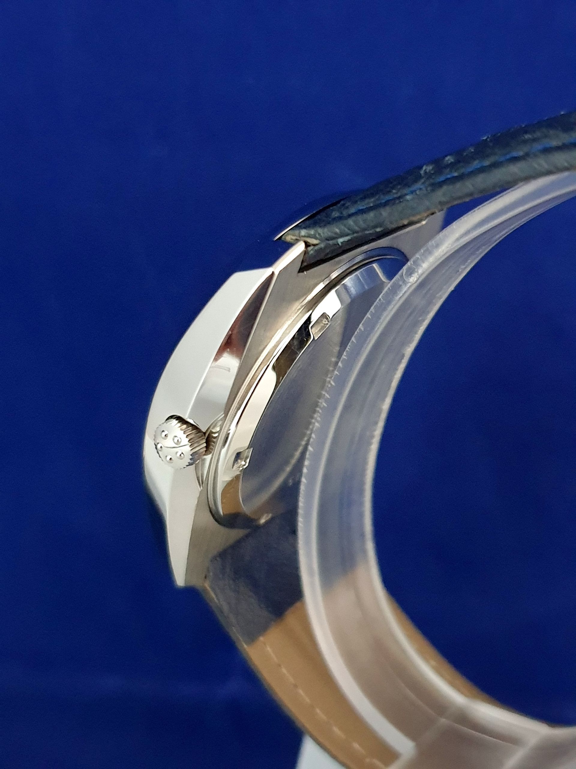 Close-up of a silver wristwatch clasp with a blue strap on a blue background