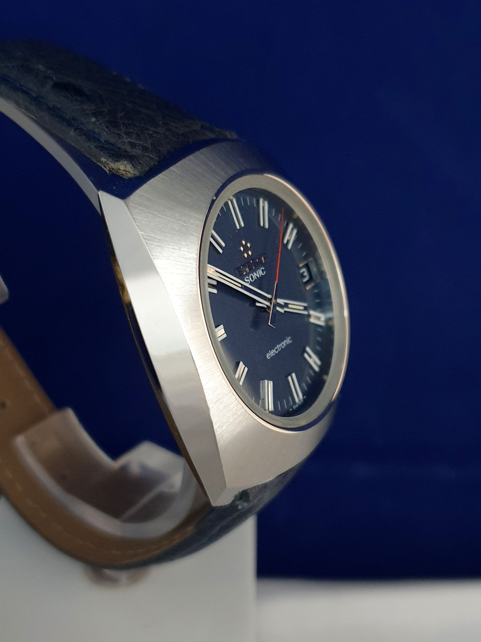 Close-up of a silver wristwatch with a dark blue dial and strap on a display stand