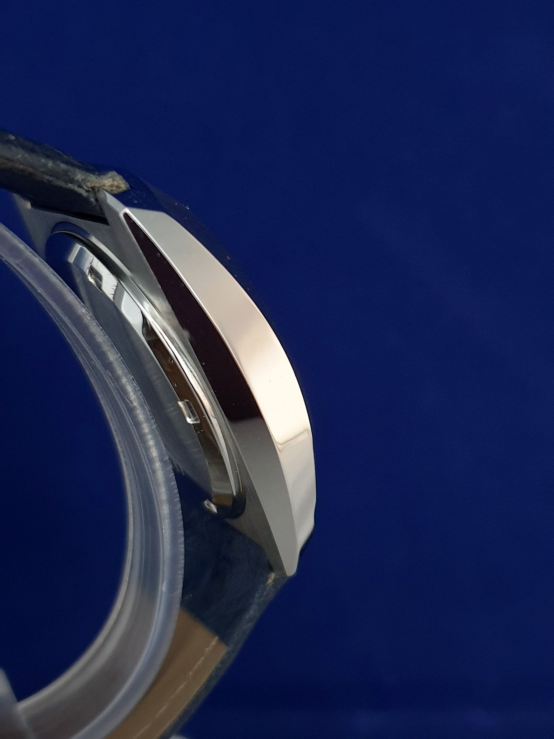 Close-up of a silver watch case and clear strap on a deep blue background
