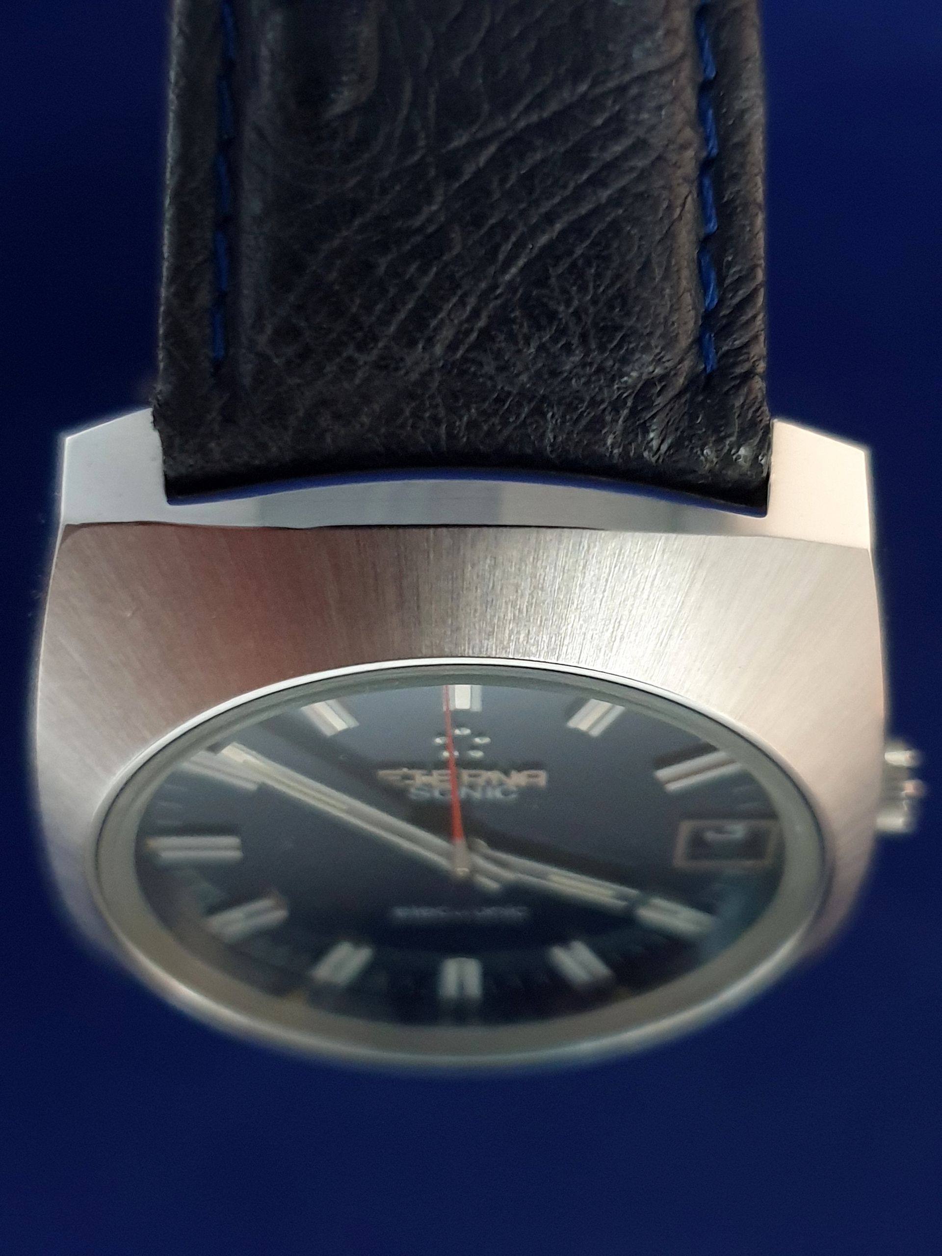 Close-up of a silver wristwatch with a black dial and black leather strap against a dark blue background