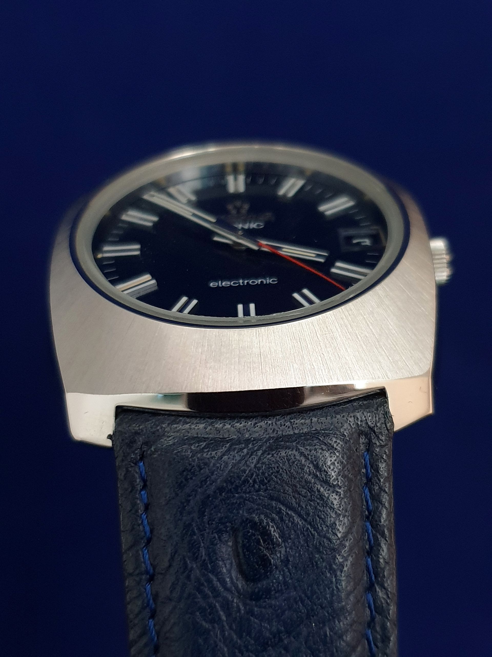 Close-up of a silver wristwatch with a black dial and black leather strap against a blue background