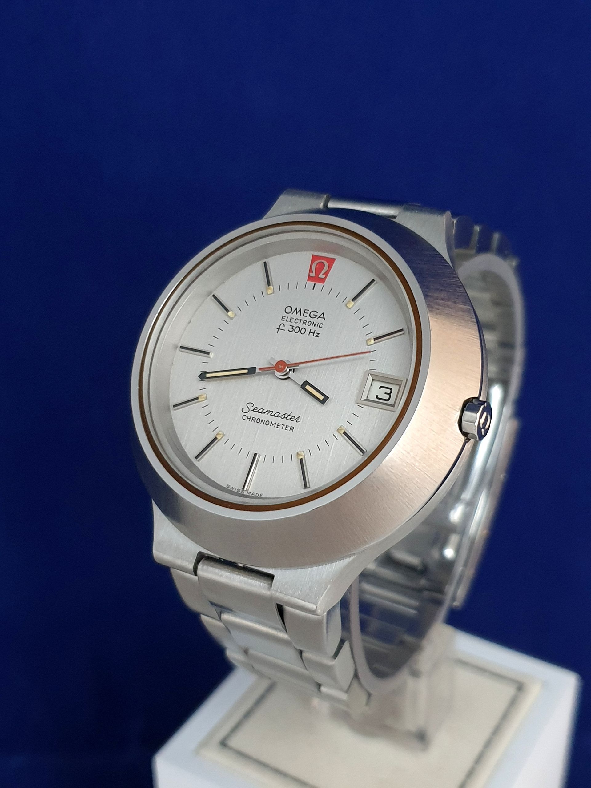 Silver wristwatch with white dial on a display stand against a blue background
