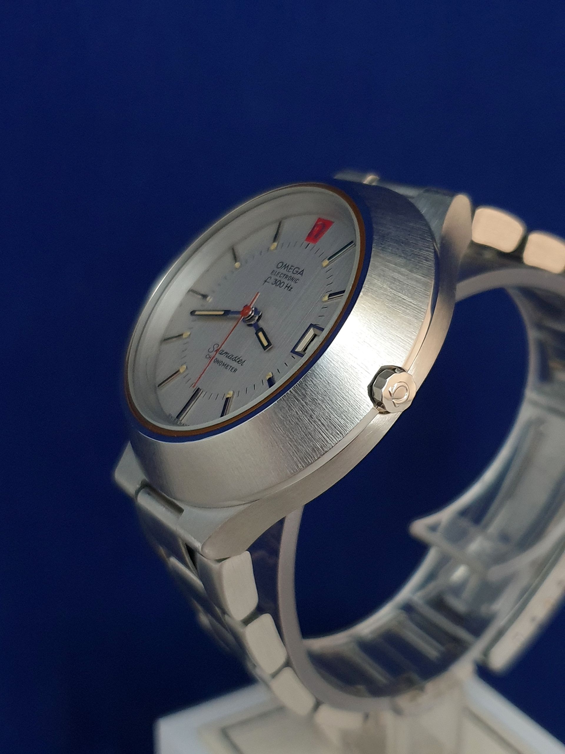 Silver wristwatch with white dial and red accent on a blue background