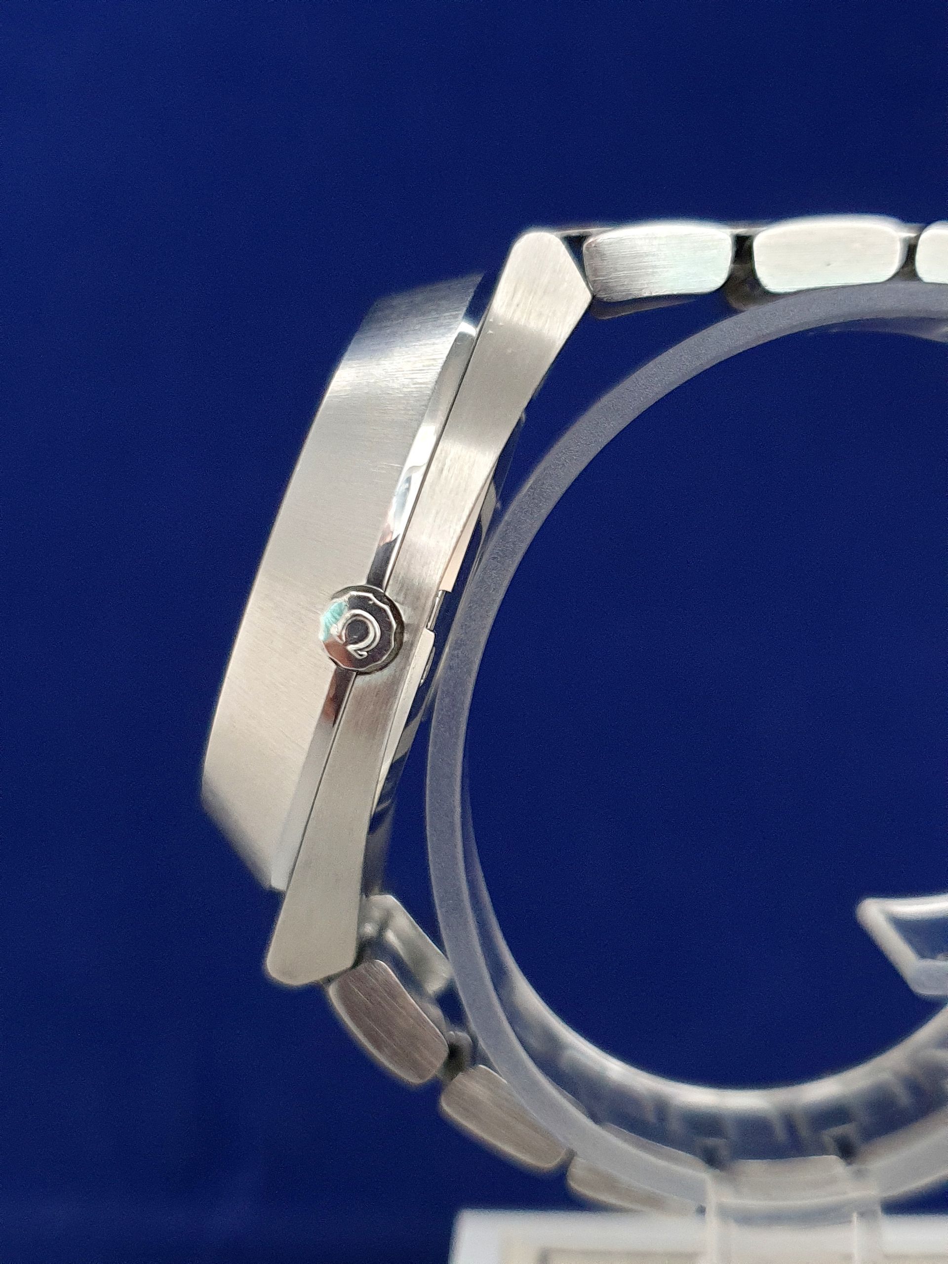 Close-up of a silver wristwatch side profile on a clear stand against a blue background