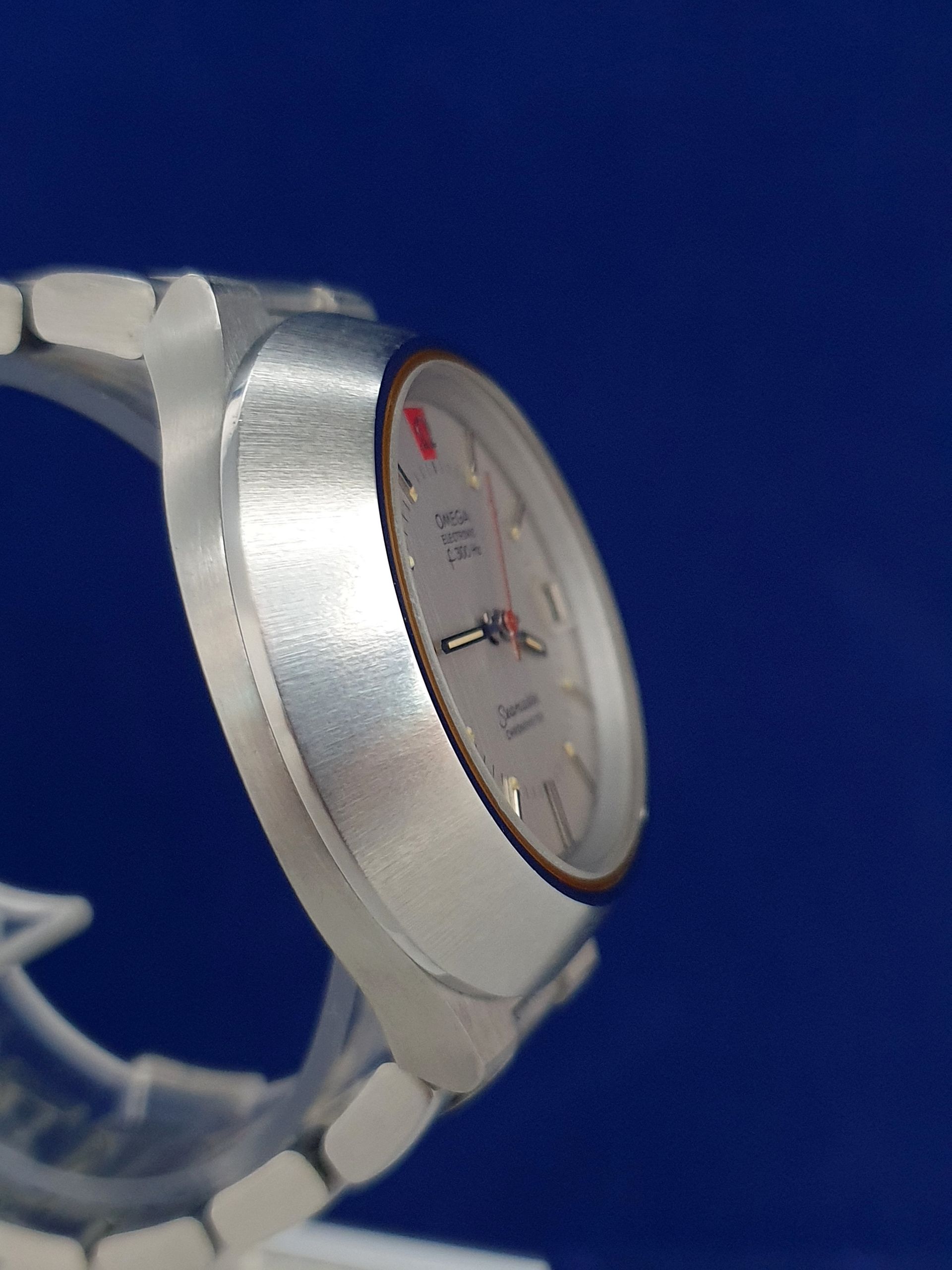 Close-up of a silver wristwatch with a white face and red accents on a blue background