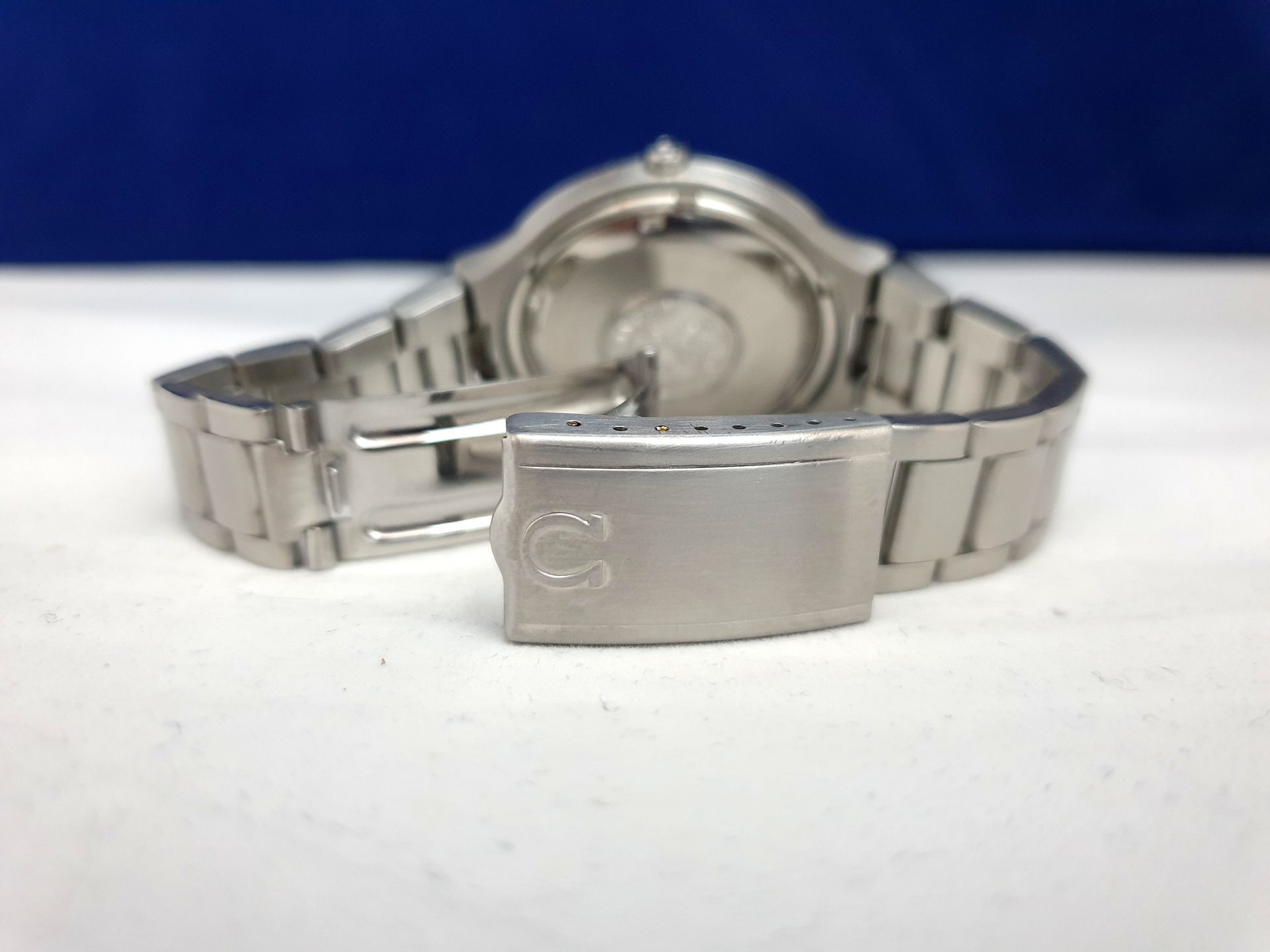 Silver metal wristwatch with a clasp, shown from the back against a blue and white background