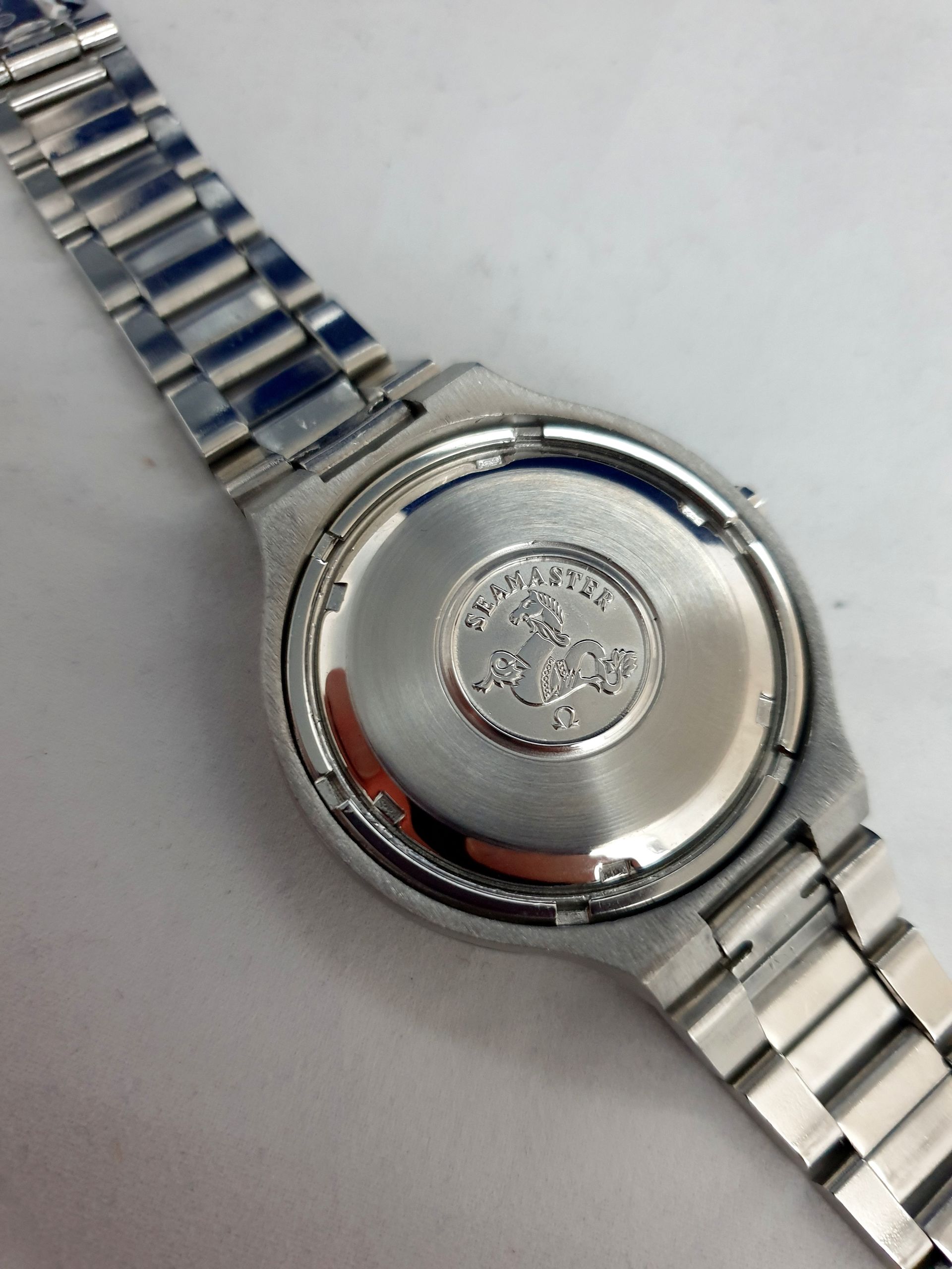 Close-up of a silver wristwatch back with metal link band on a white surface