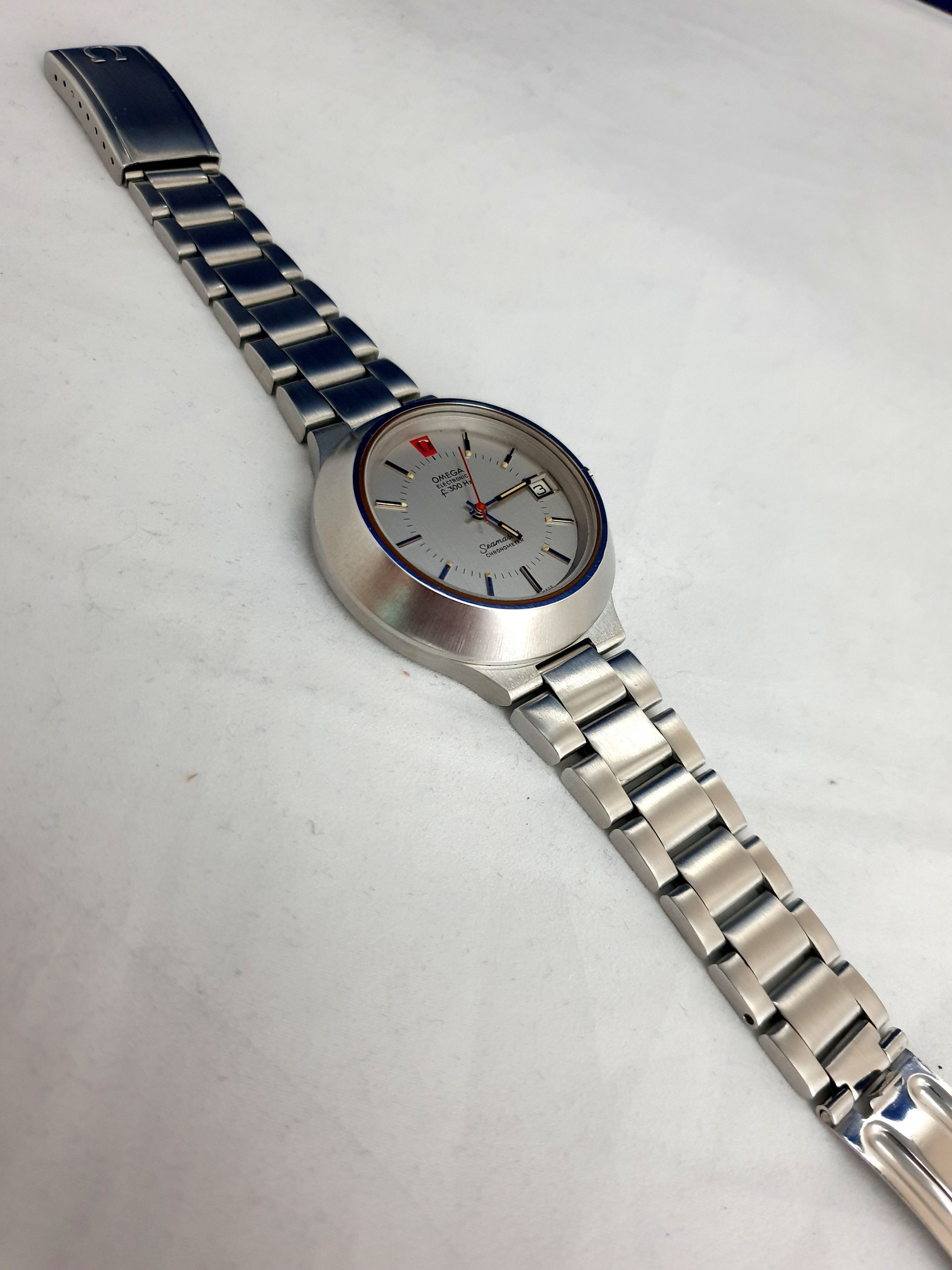 Silver wristwatch with a blue metal band on a white surface