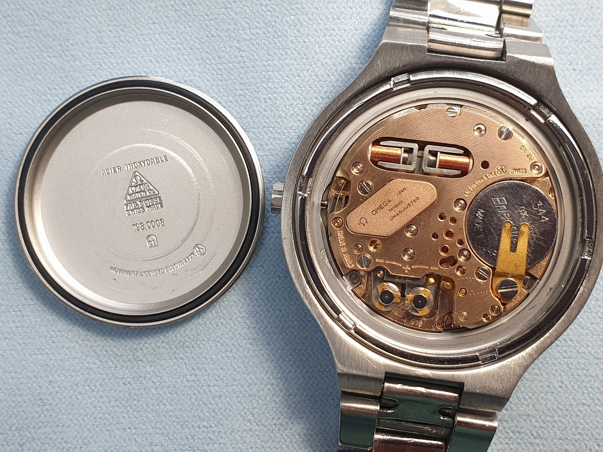 Open watch case showing exposed movement beside the removed back cover on a blue surface