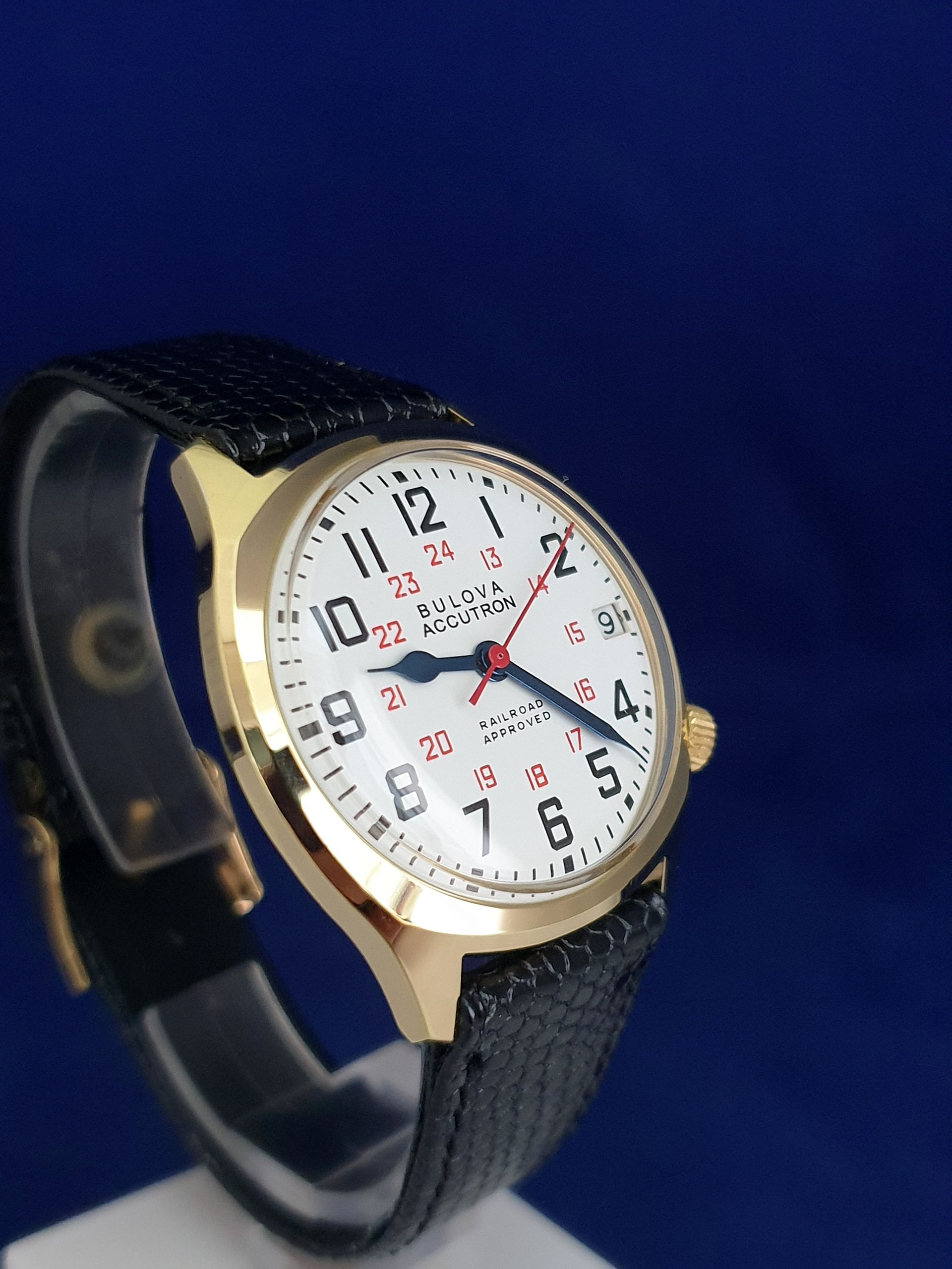 Gold wristwatch with white dial and black strap on a blue background