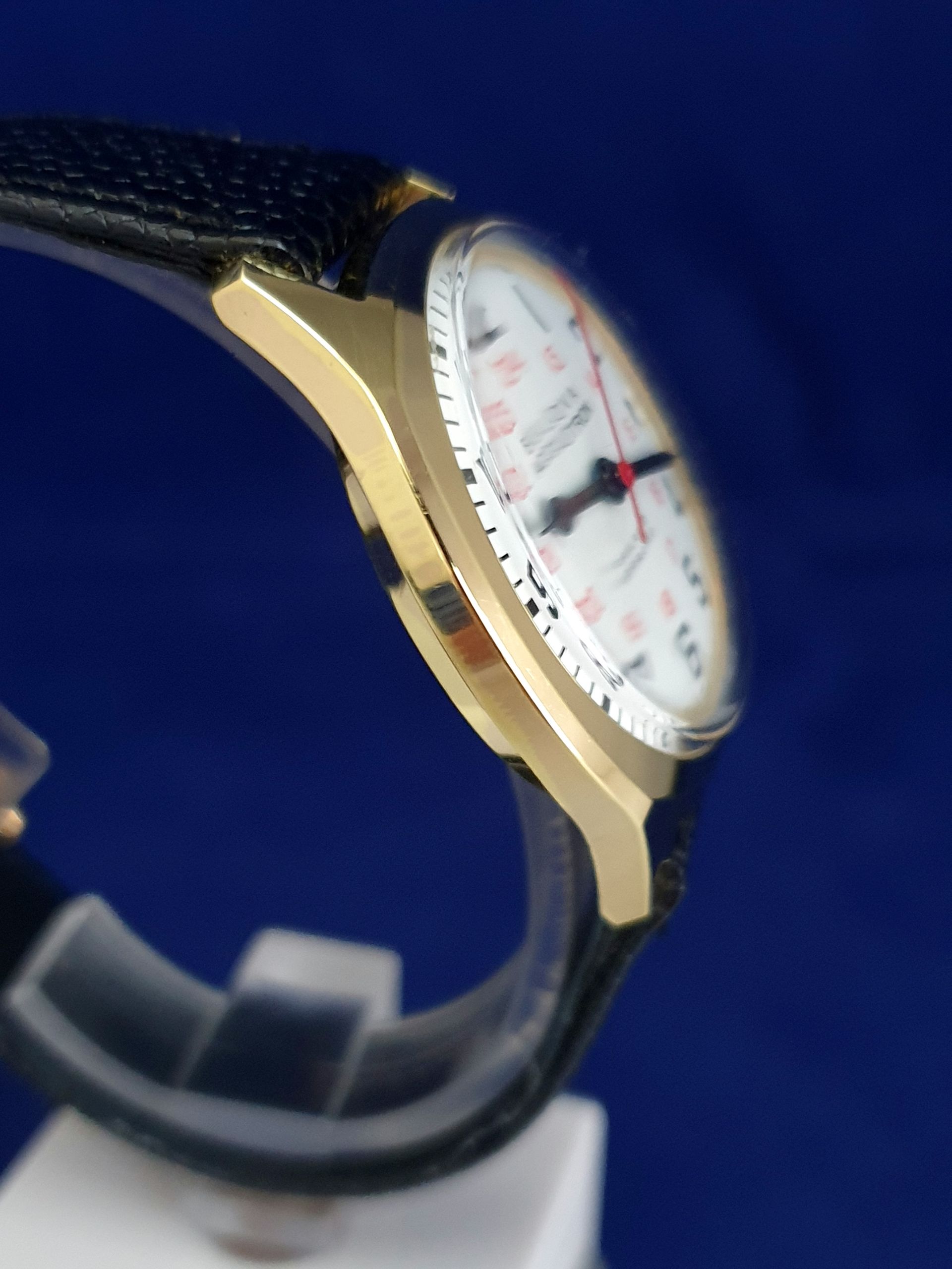 Close-up of a gold wristwatch with a black strap and white face against a blue background