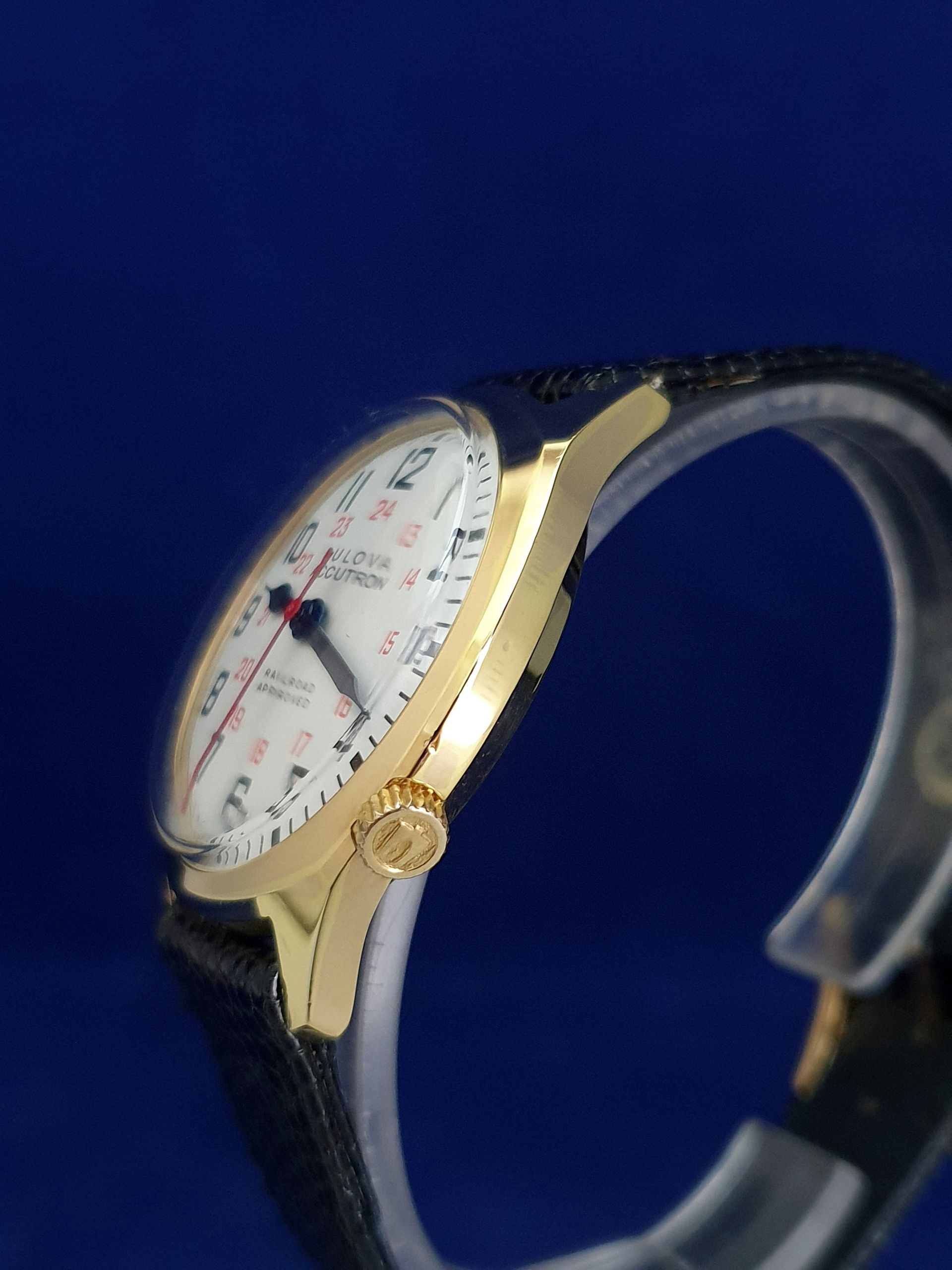 Gold wristwatch with white face and black leather band on a blue background