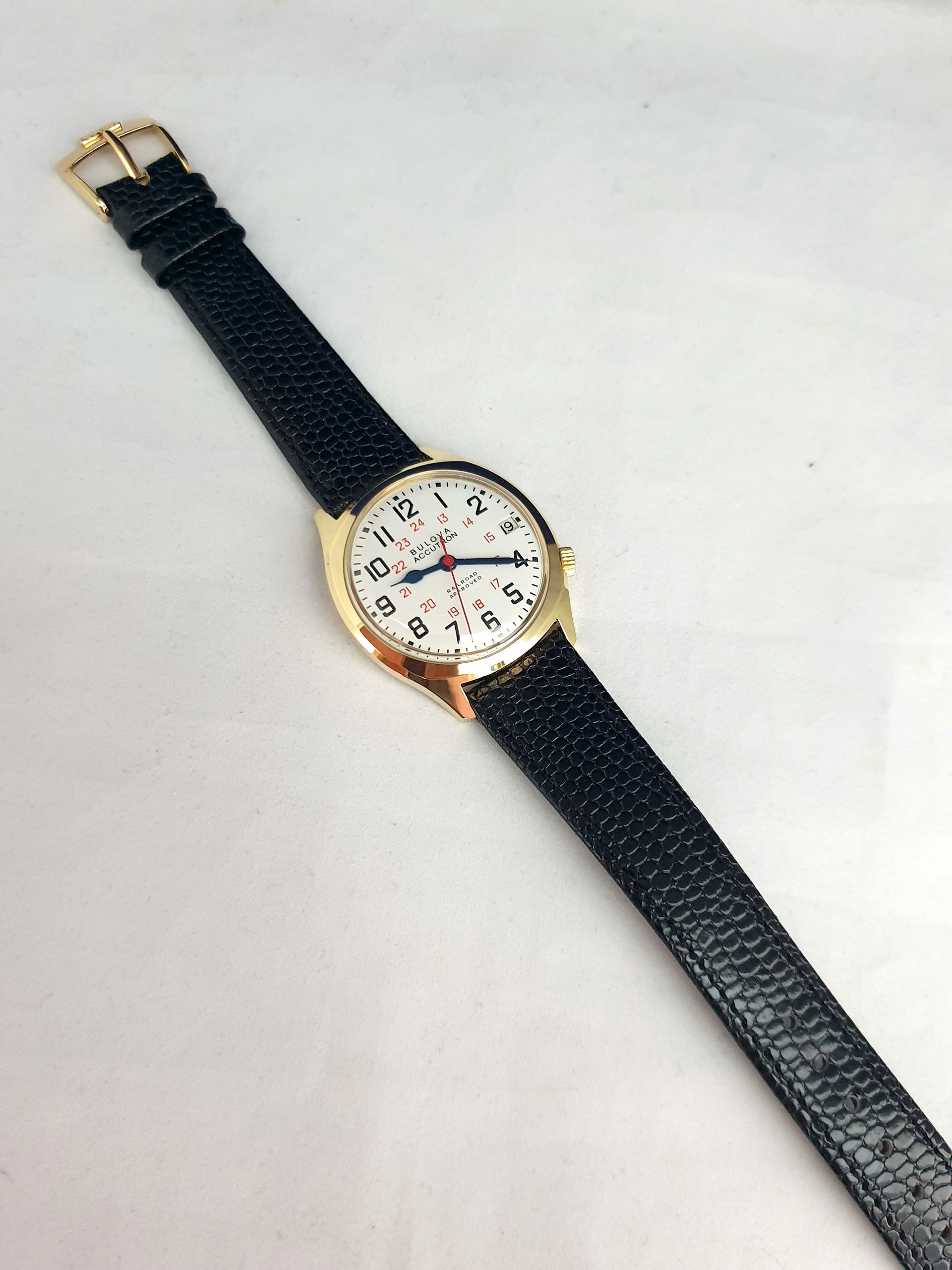Gold wristwatch with black strap on a light background