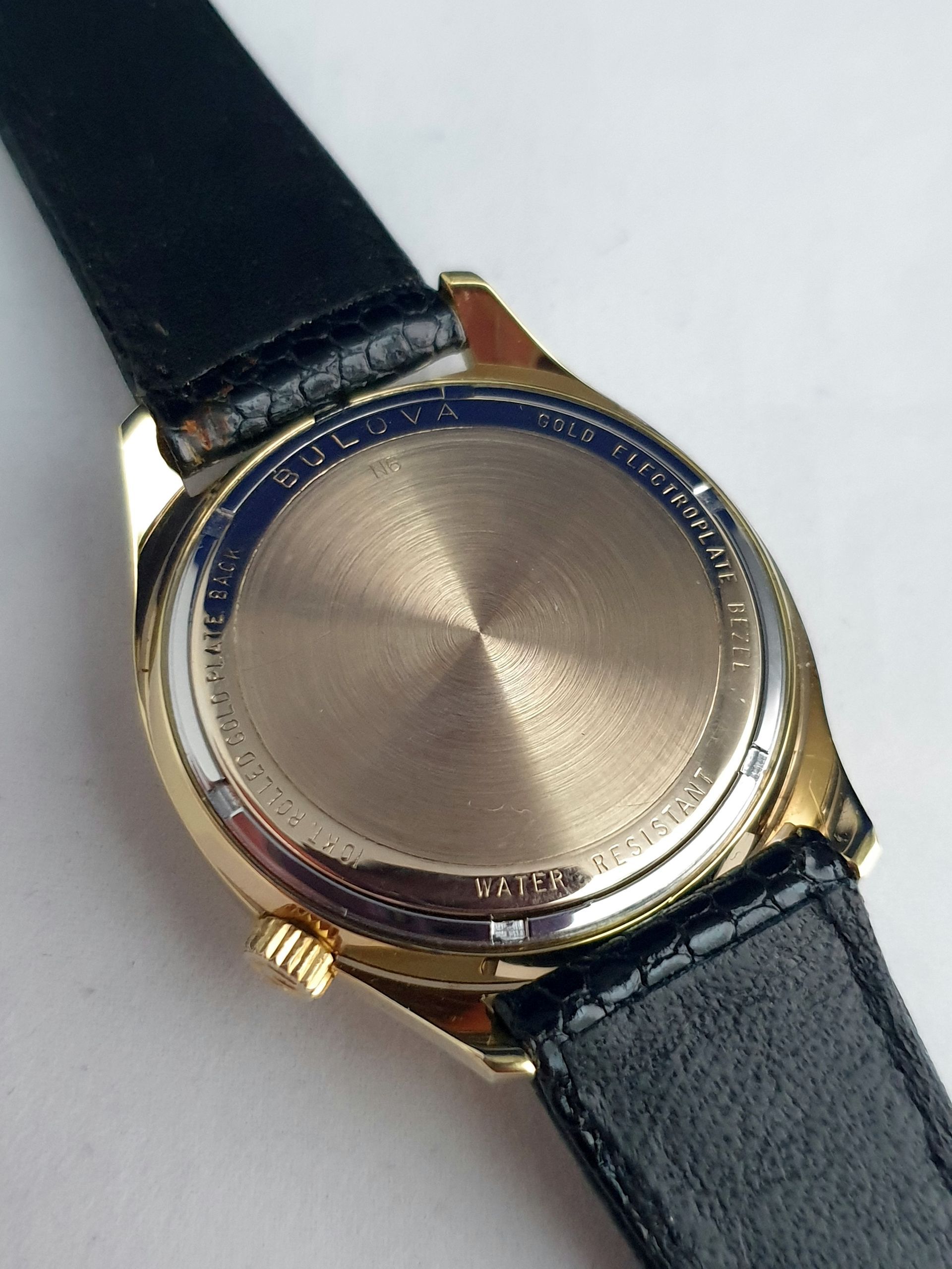 Back view of a gold-tone wristwatch with a black leather strap and round brushed case back.