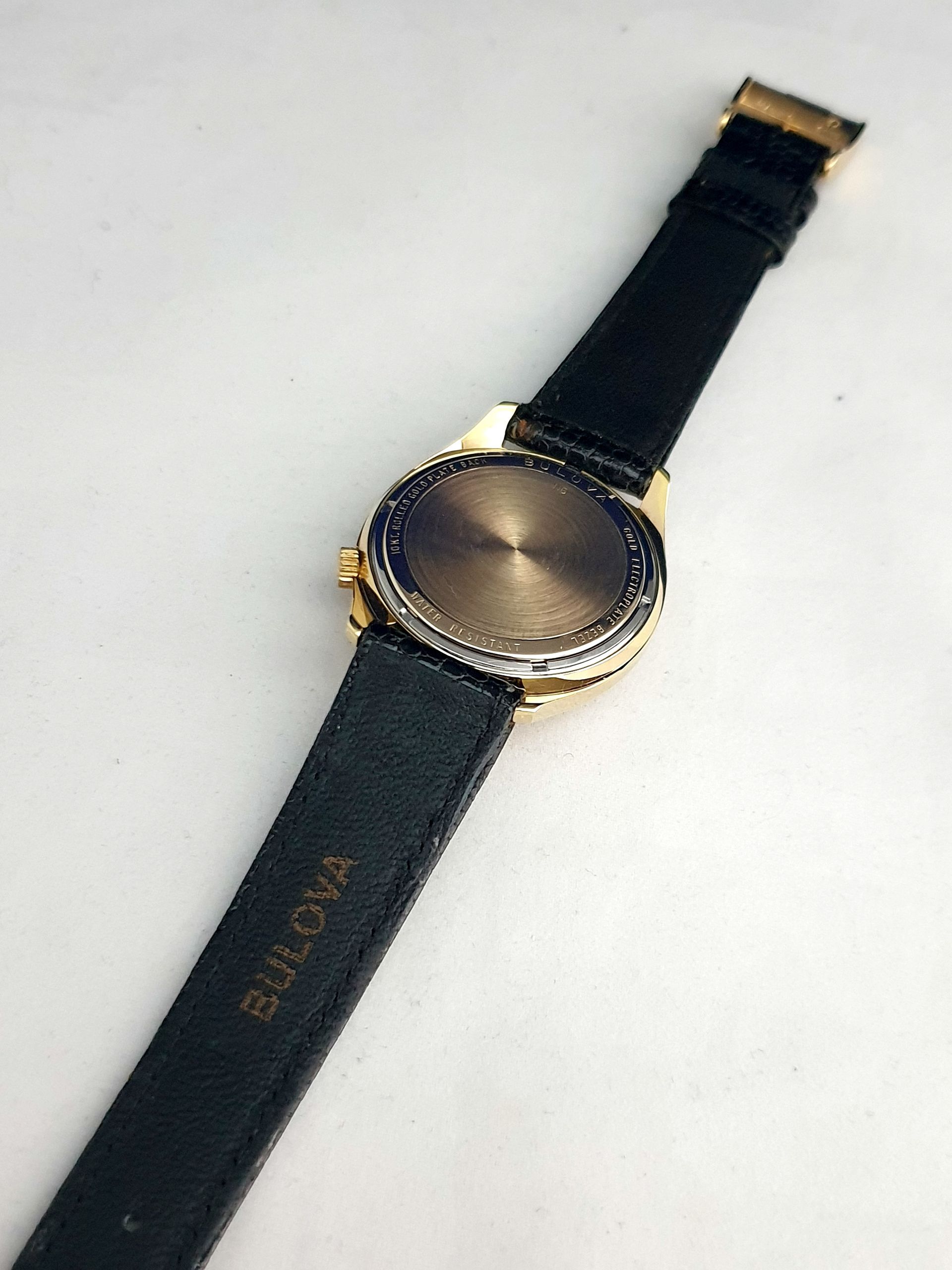 Black watch with gold bezel and strap, shown face down on a light surface