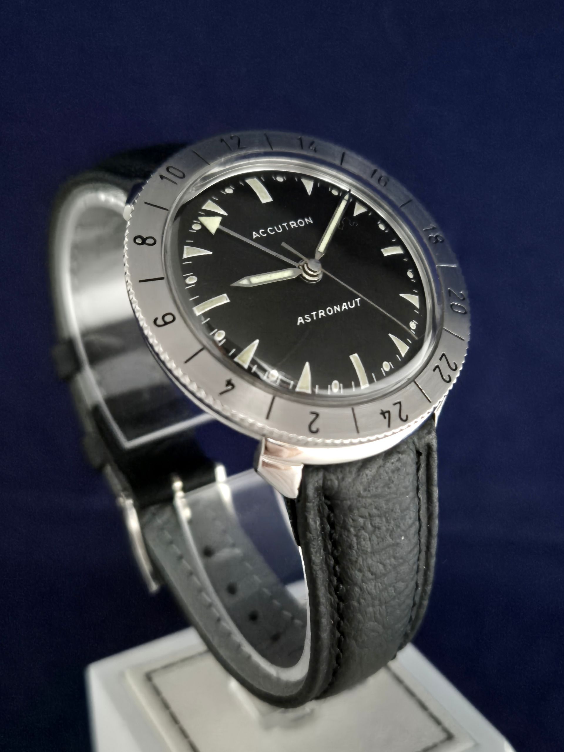 Black wristwatch with silver bezel and leather strap on a dark blue background