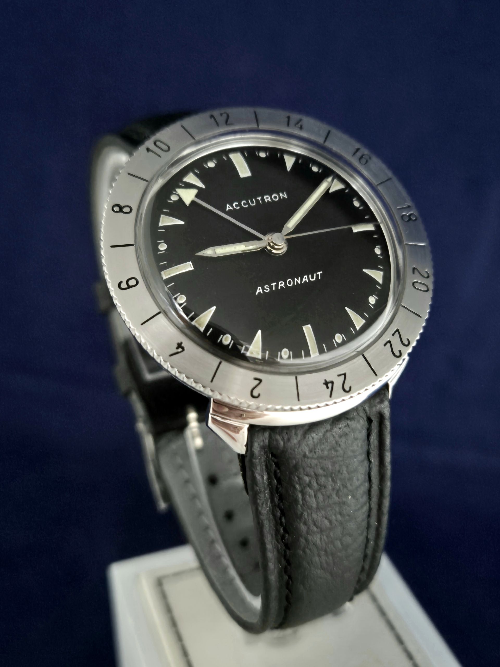 Black leather strap watch with silver bezel and black dial on a stand