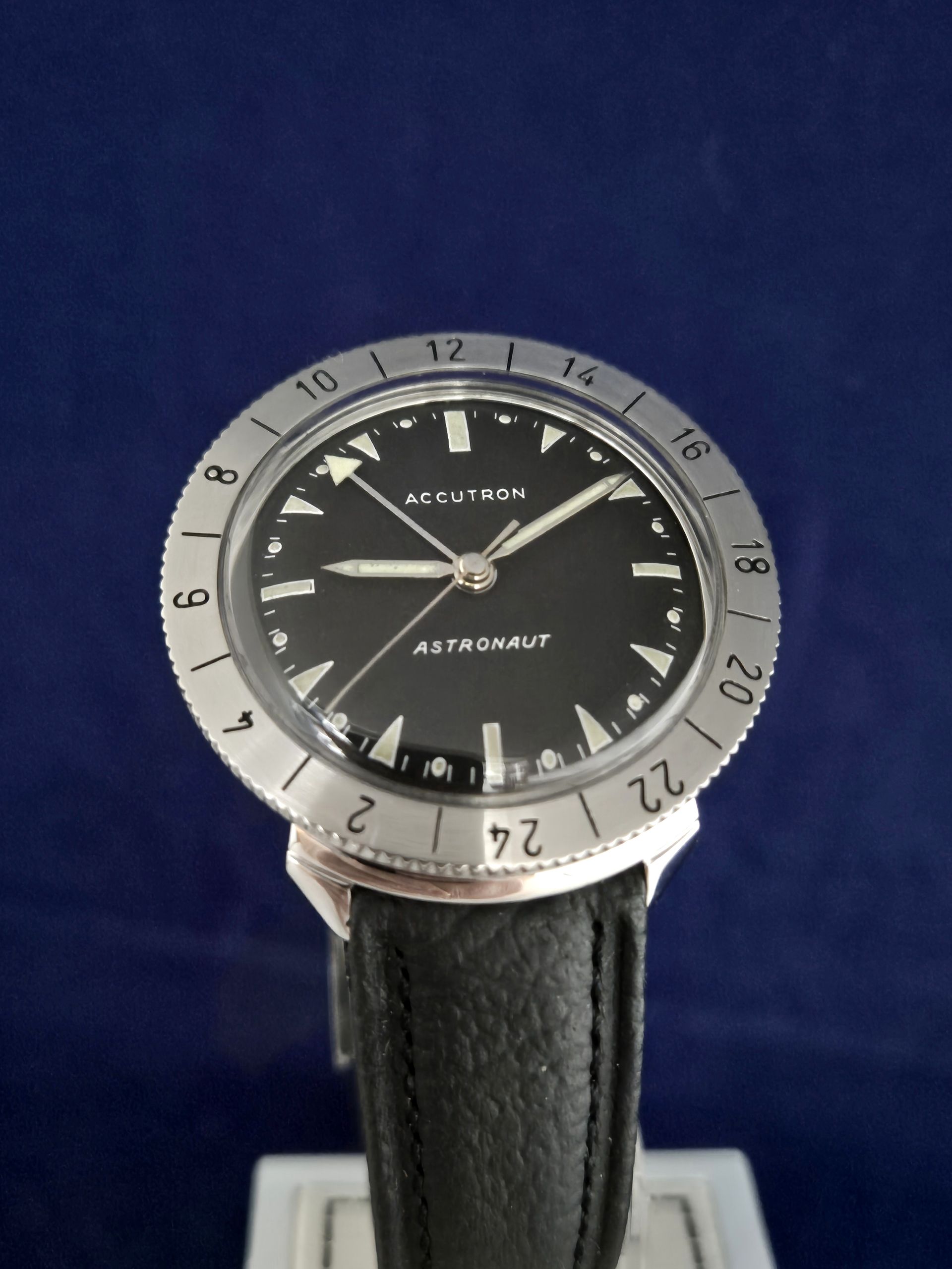 Silver and black wristwatch with a leather strap against a blue background