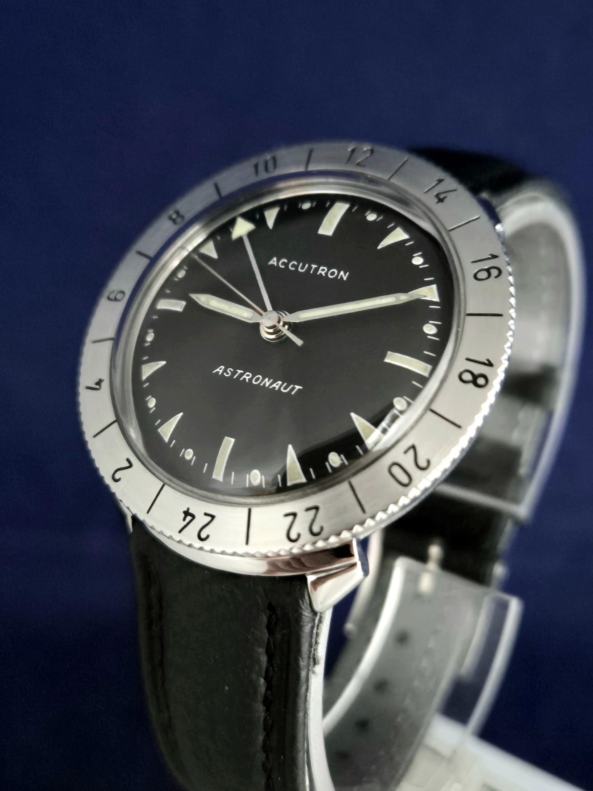Close-up of a black wristwatch with a silver bezel and leather strap on a blue background
