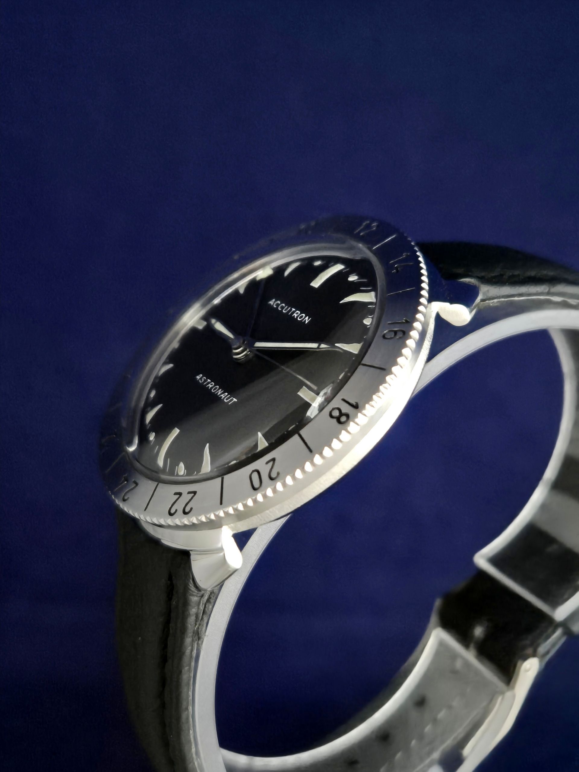 Close-up of a silver-and-black wristwatch with a black dial on a blue background