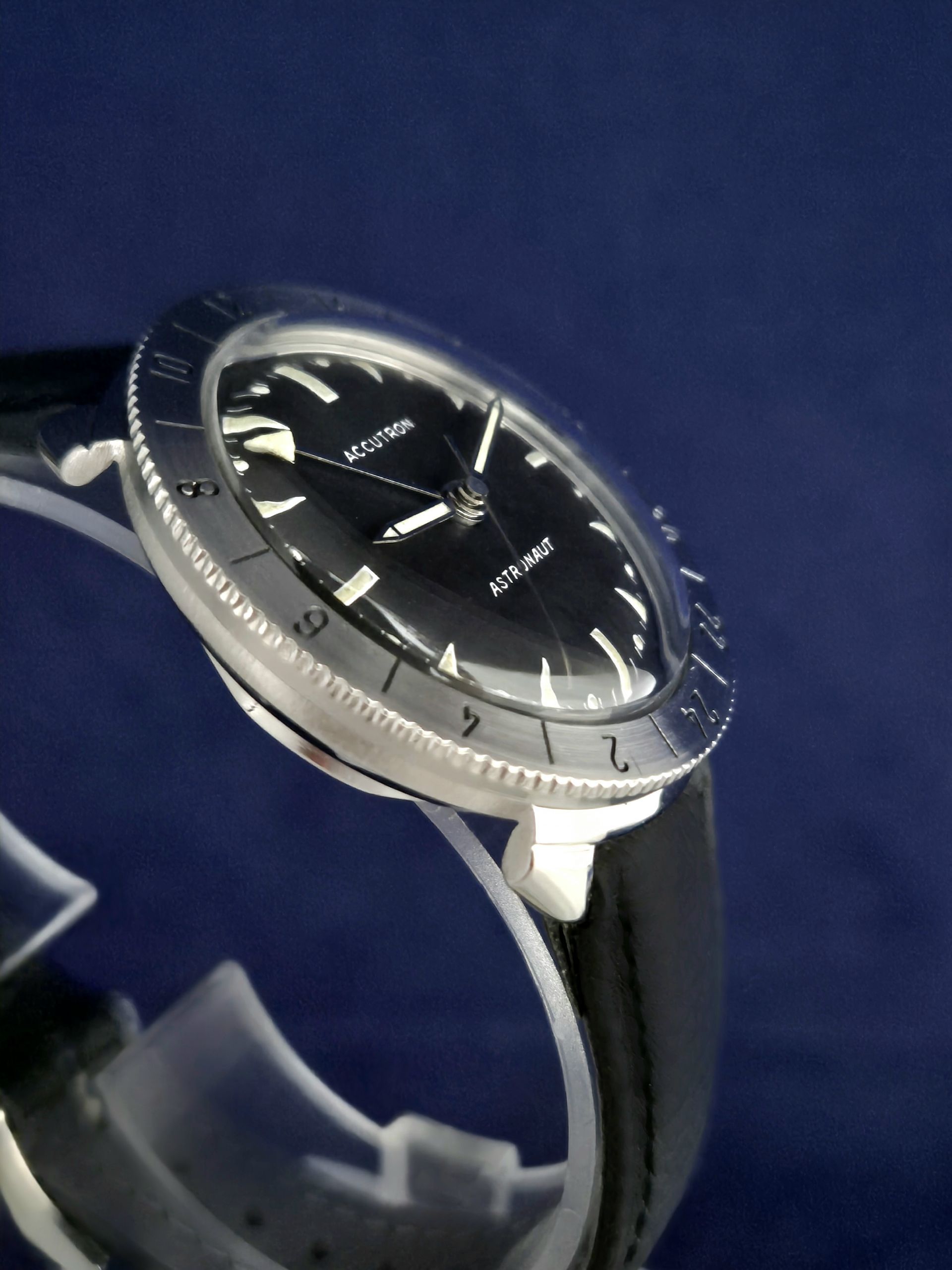 Close-up of a black wristwatch with a silver bezel and black strap on a blue background